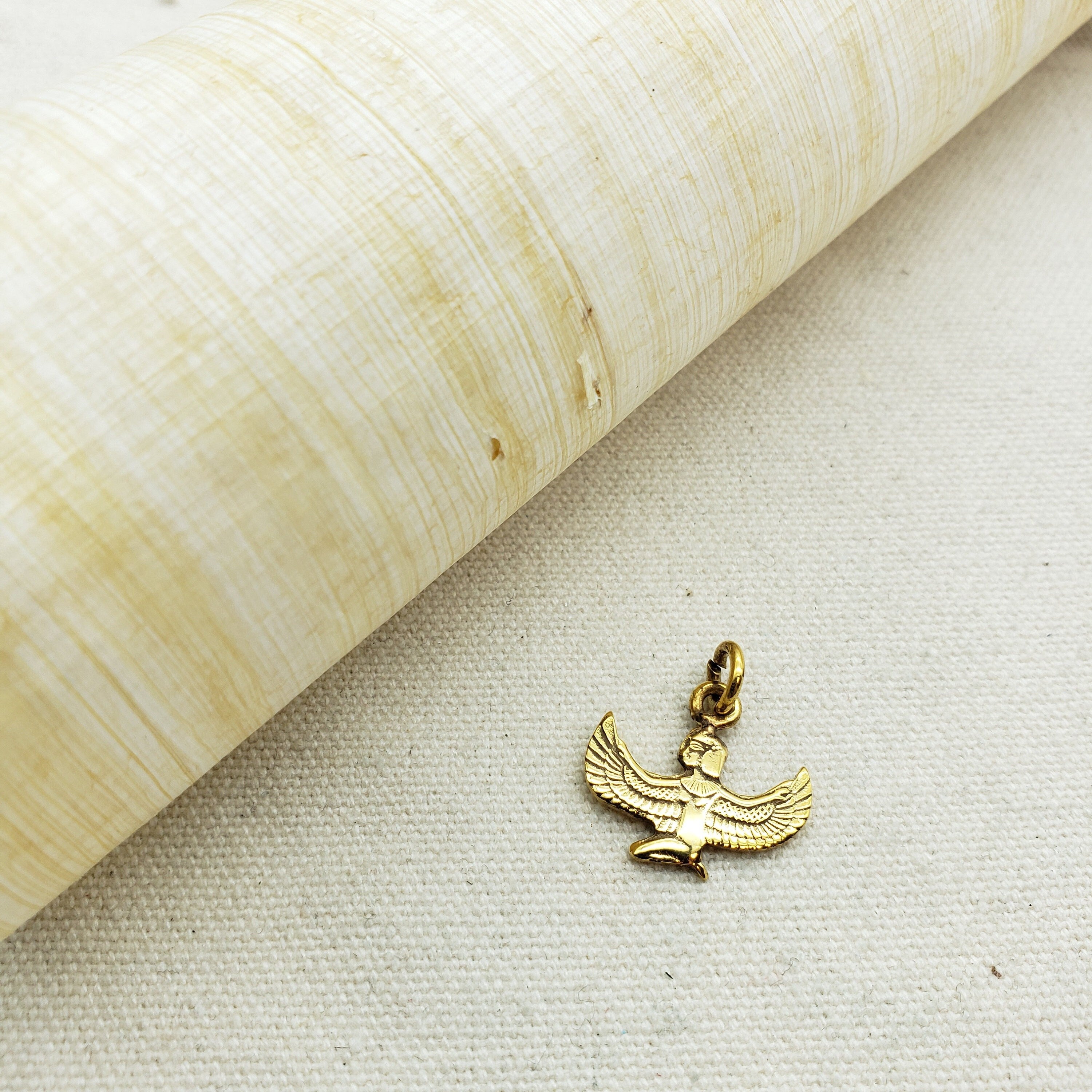 A gold-plated Egyptian goddess Isis pendant made of gold-plated Egyptian silver, displayed against a beige background.
