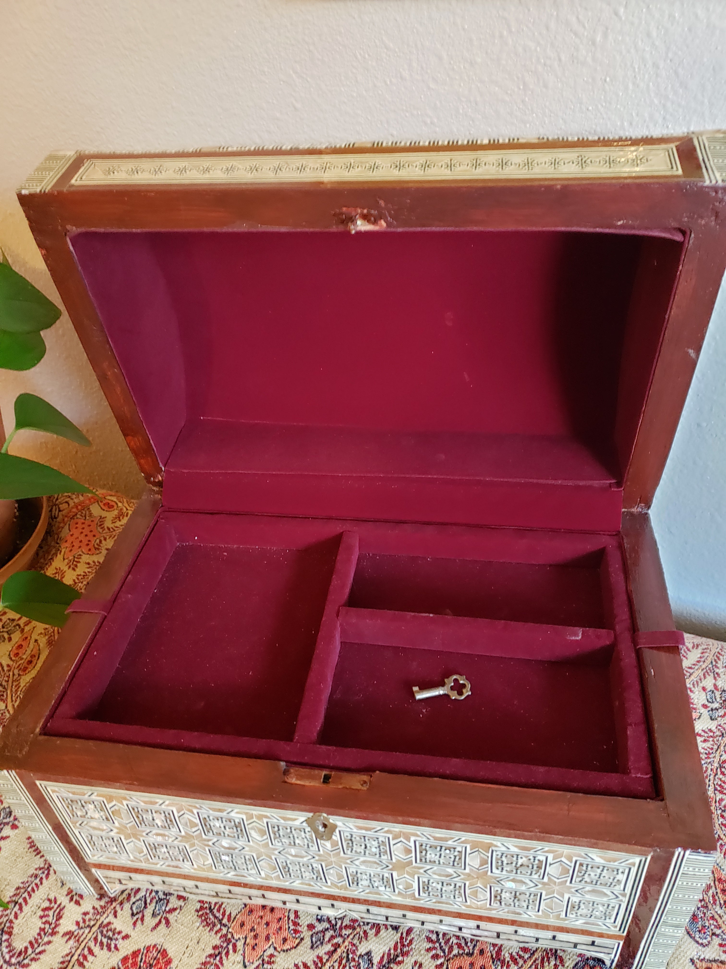 Open wooden box with red interior and key, on a patterned surface