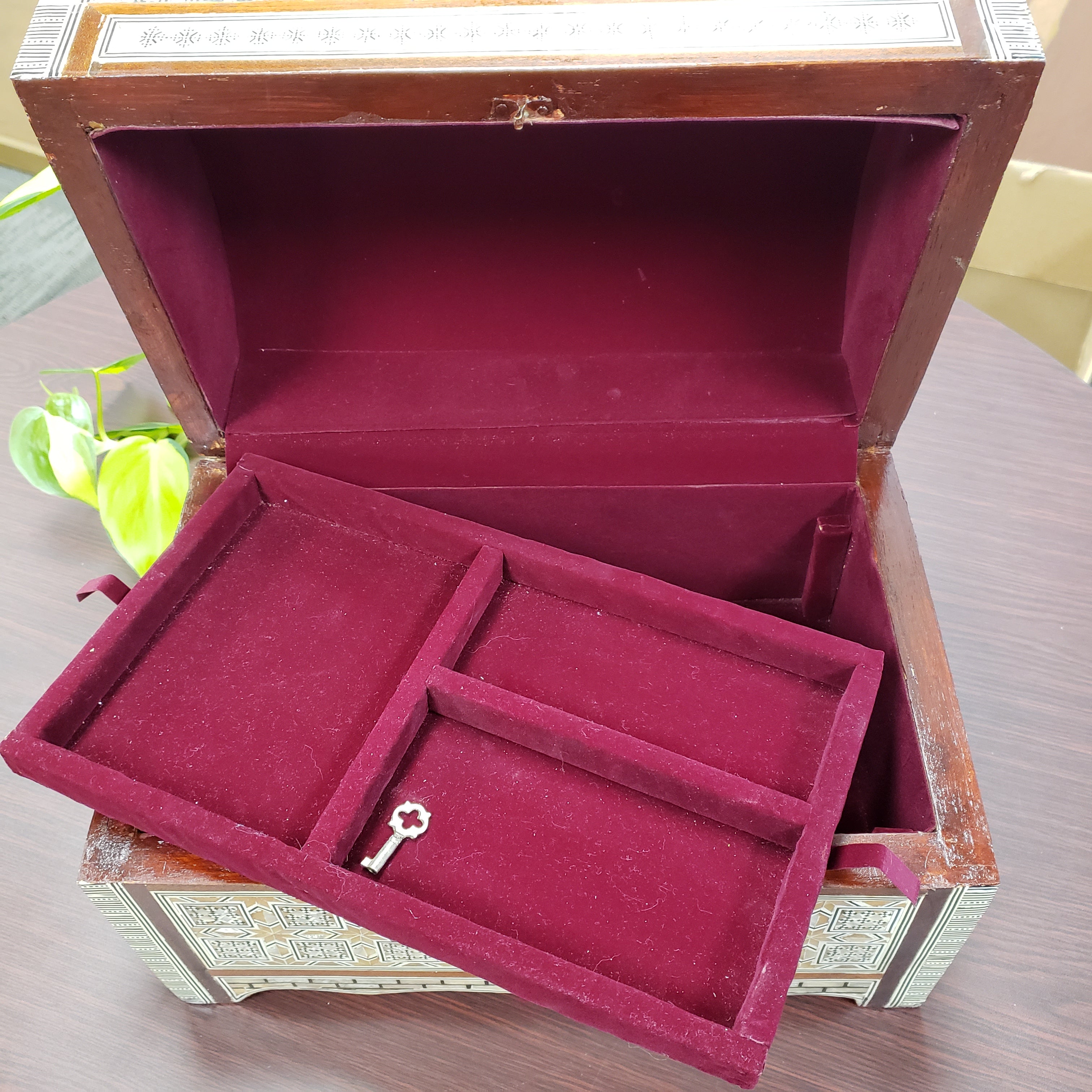 Open jewelry box with maroon interior and key-shaped object on a wooden surface.
