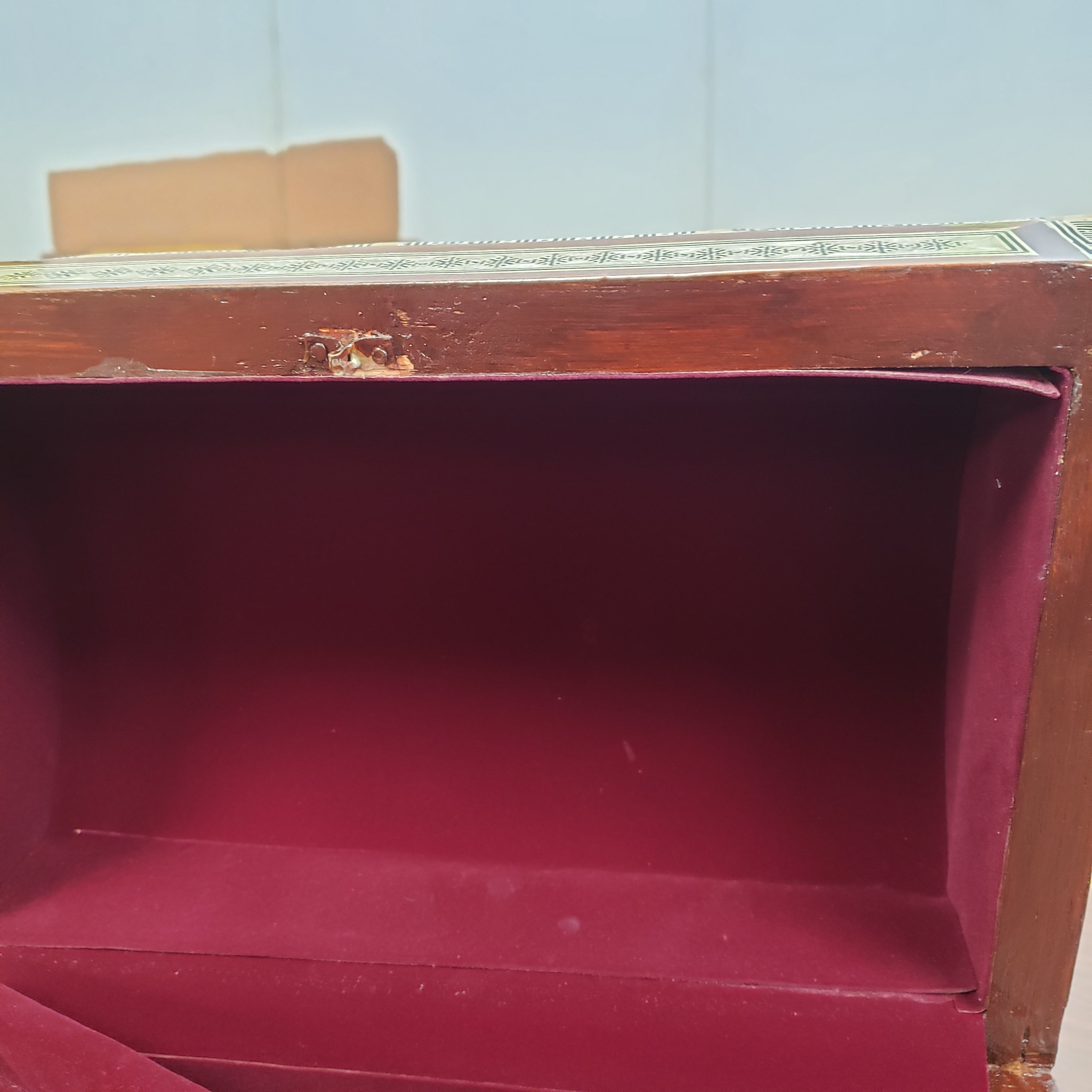 Close-up of a wooden box with a red interior against a light blue wall.