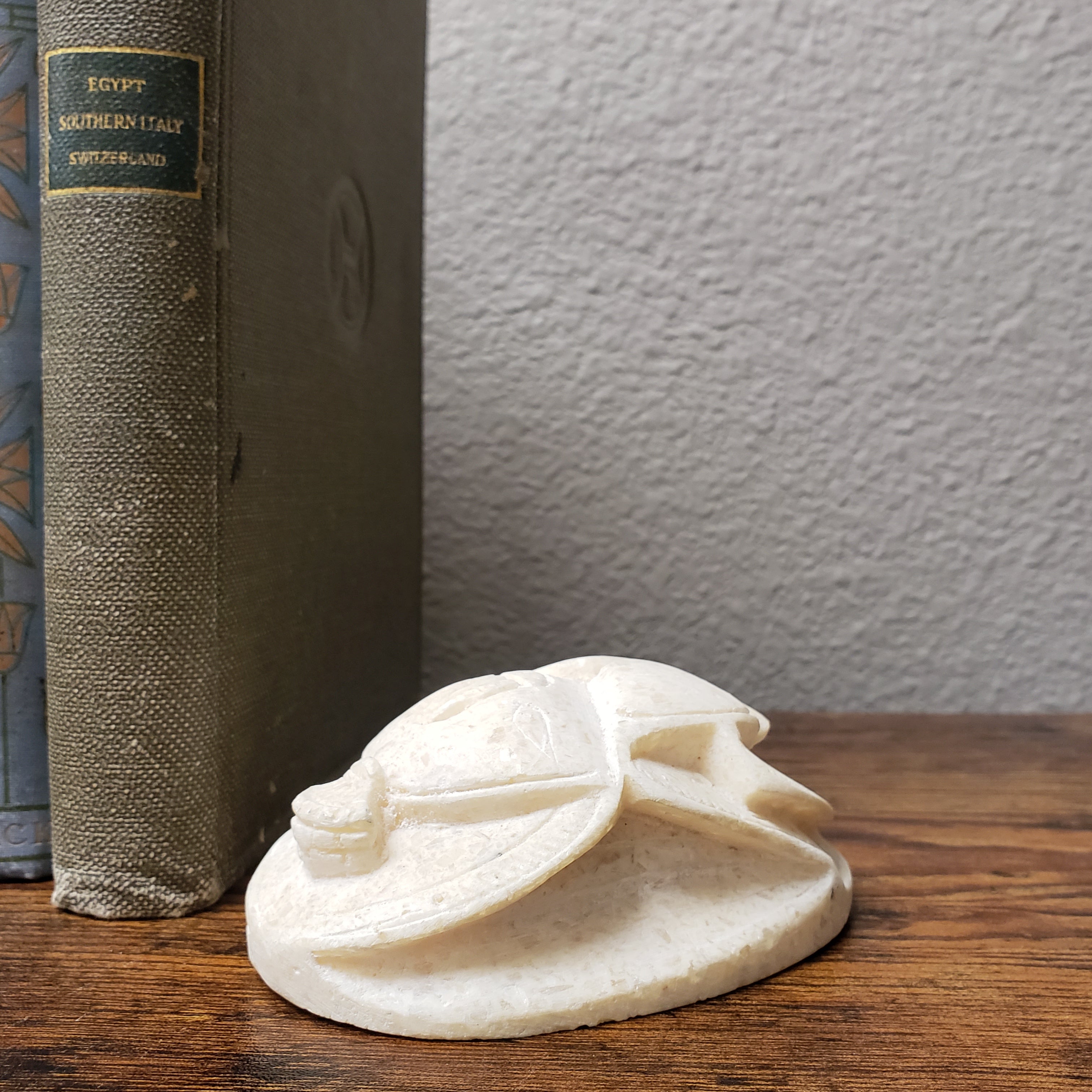 Small white sculpture on top of a book with a wooden surface and white wall in the background