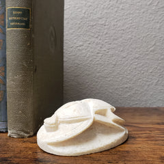 Small white sculpture on top of a book with a wooden surface and white wall in the background