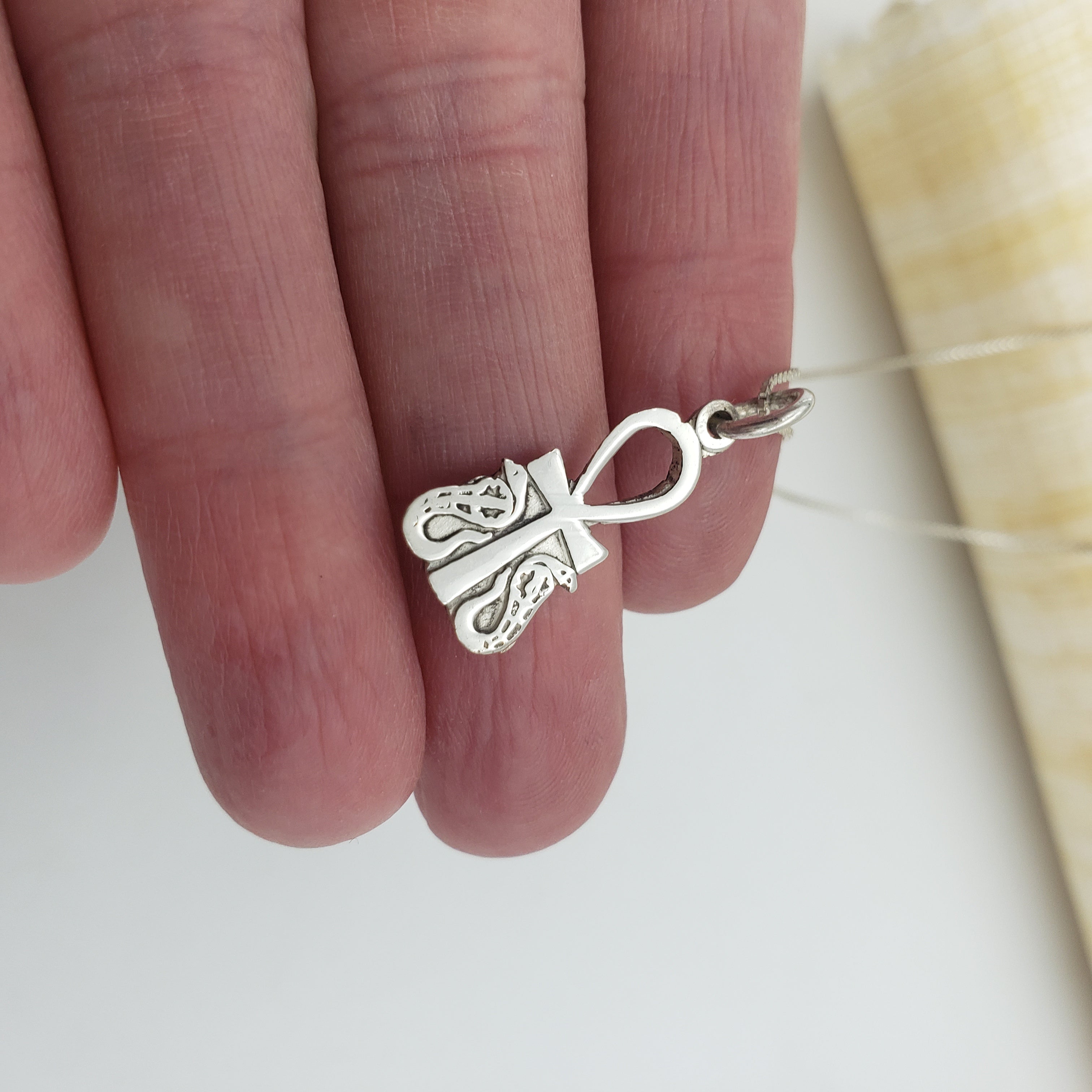 Silver an ankh and cobra pendant held between fingers on a neutral background