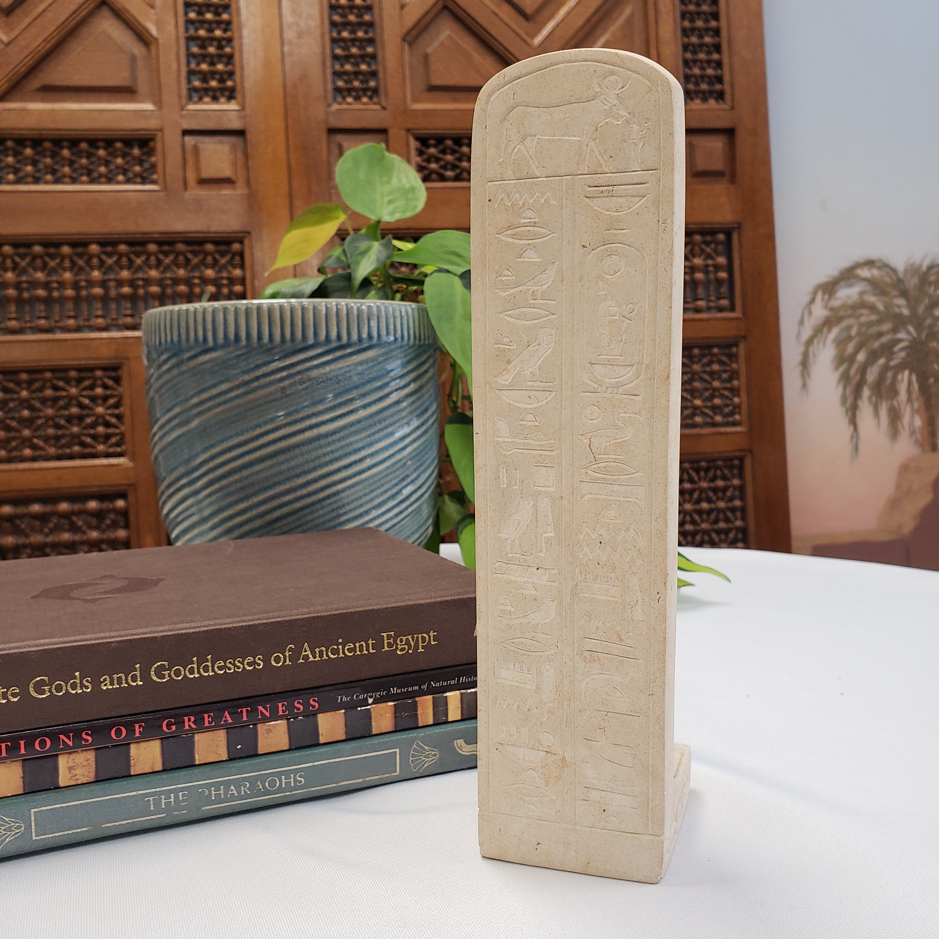 Decorative stone slab with hieroglyphics on a surface with books and plants in the background