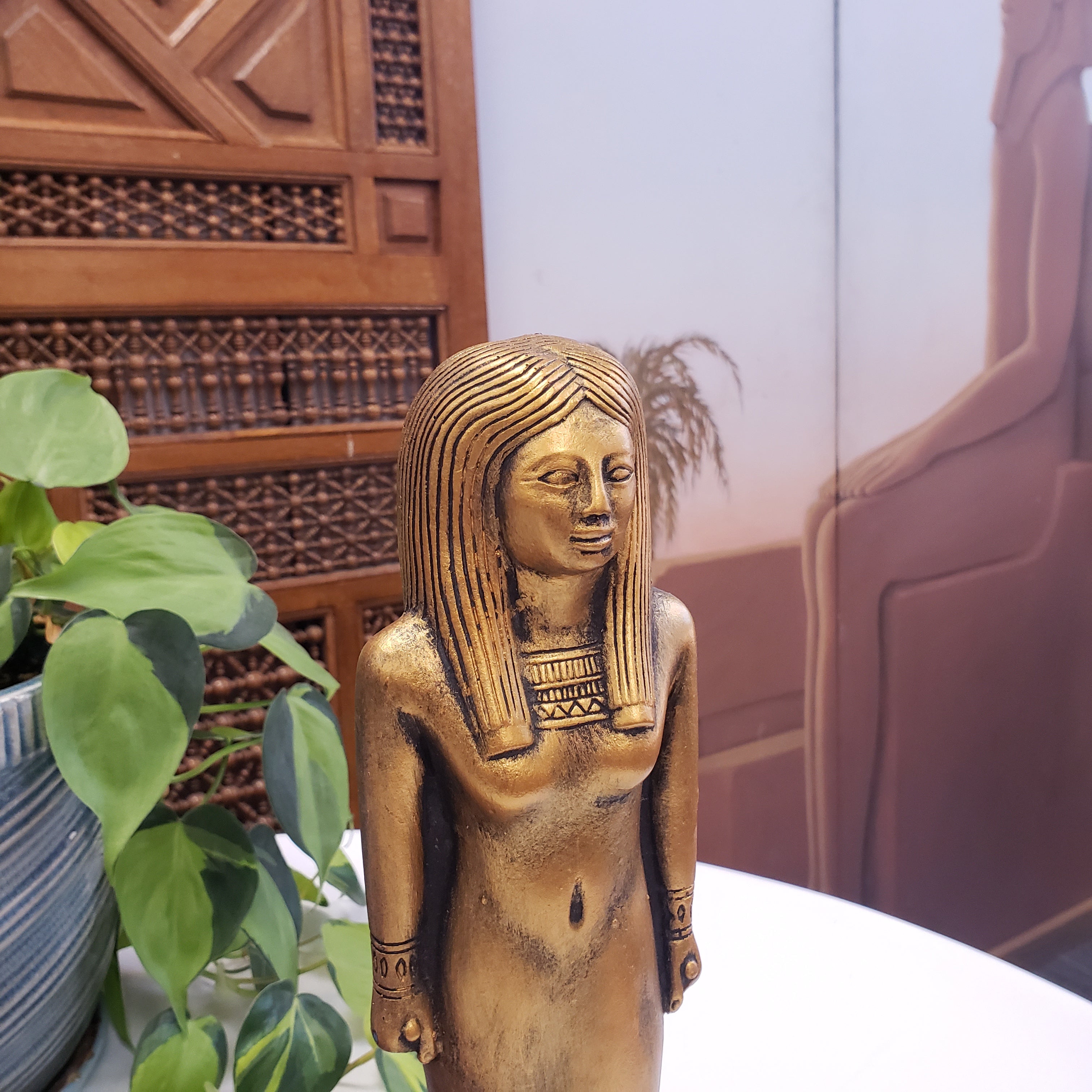 Statue with decorative patterns, placed indoors with plants and wooden paneling.