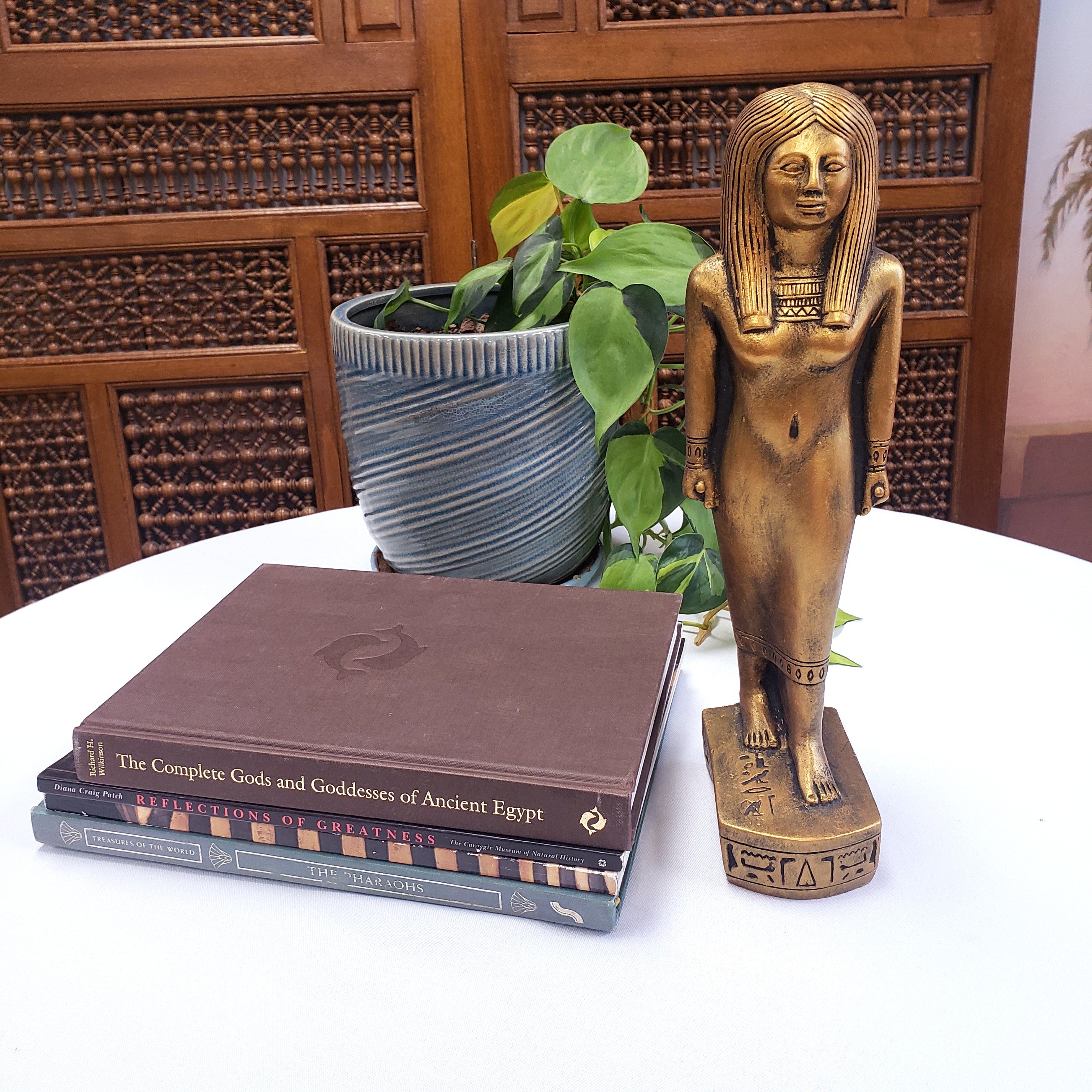 Bronze statue of an Egyptian pharaoh next to books on a table with a plant in the background