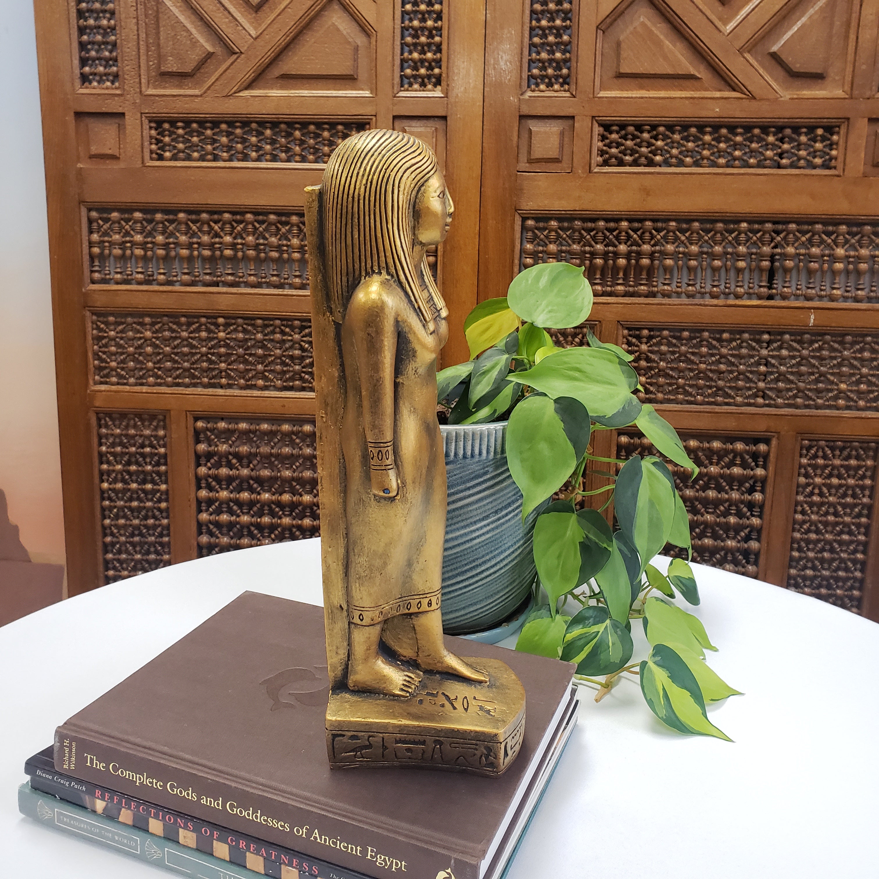 Bronze statue of a hand holding a book with a decorative wooden panel and plant in the background