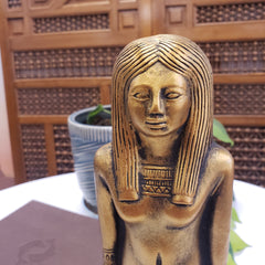 Bronze statue of a woman with intricate detailing against a wooden panel background