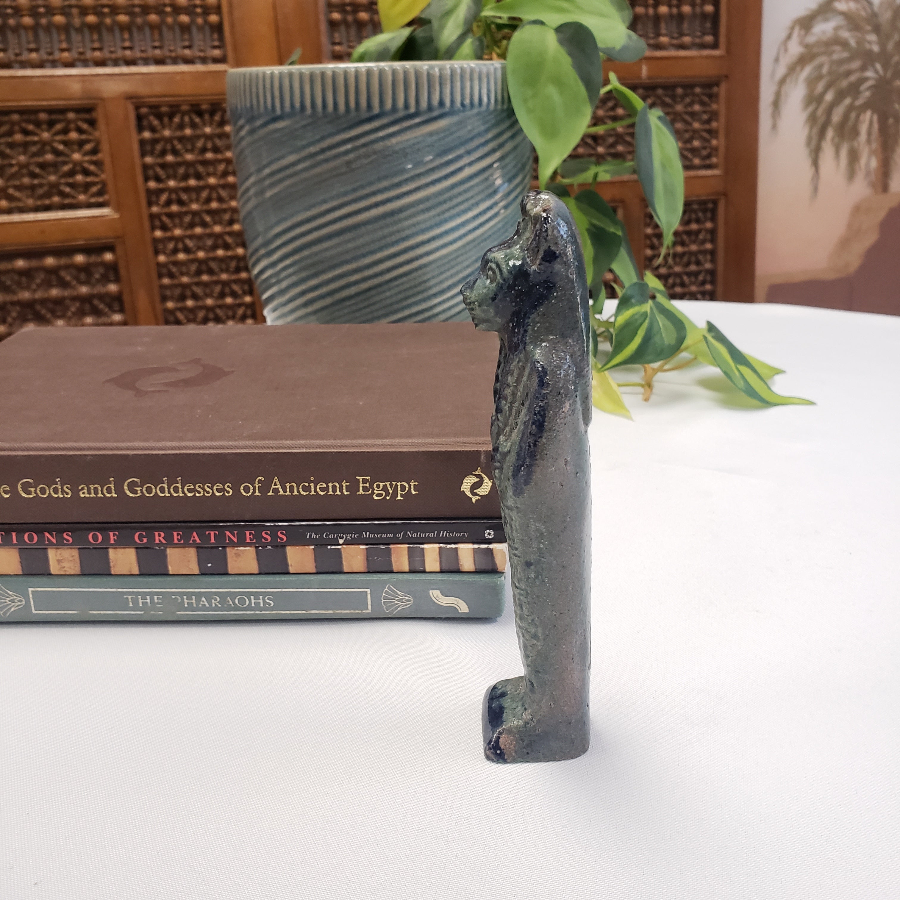 Decorative Egyptian Sekhmet figure with hieroglyphics on a book against a white wall with plants.