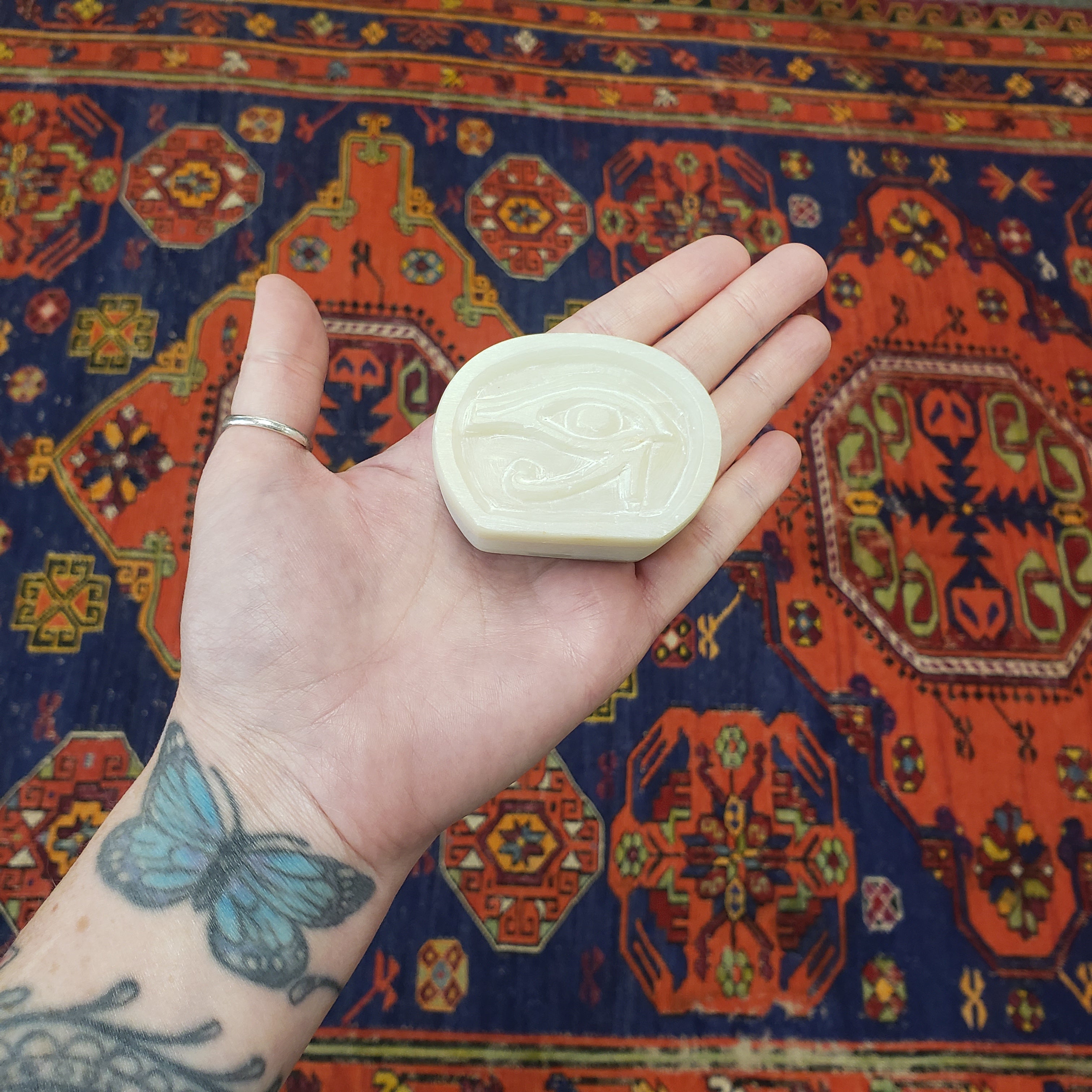 Hand holding a White soapstone box with an eye symbol against a colorful patterned rug