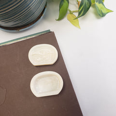 Two White soapstone box with an eye symbol on a brown book with a plant in the background