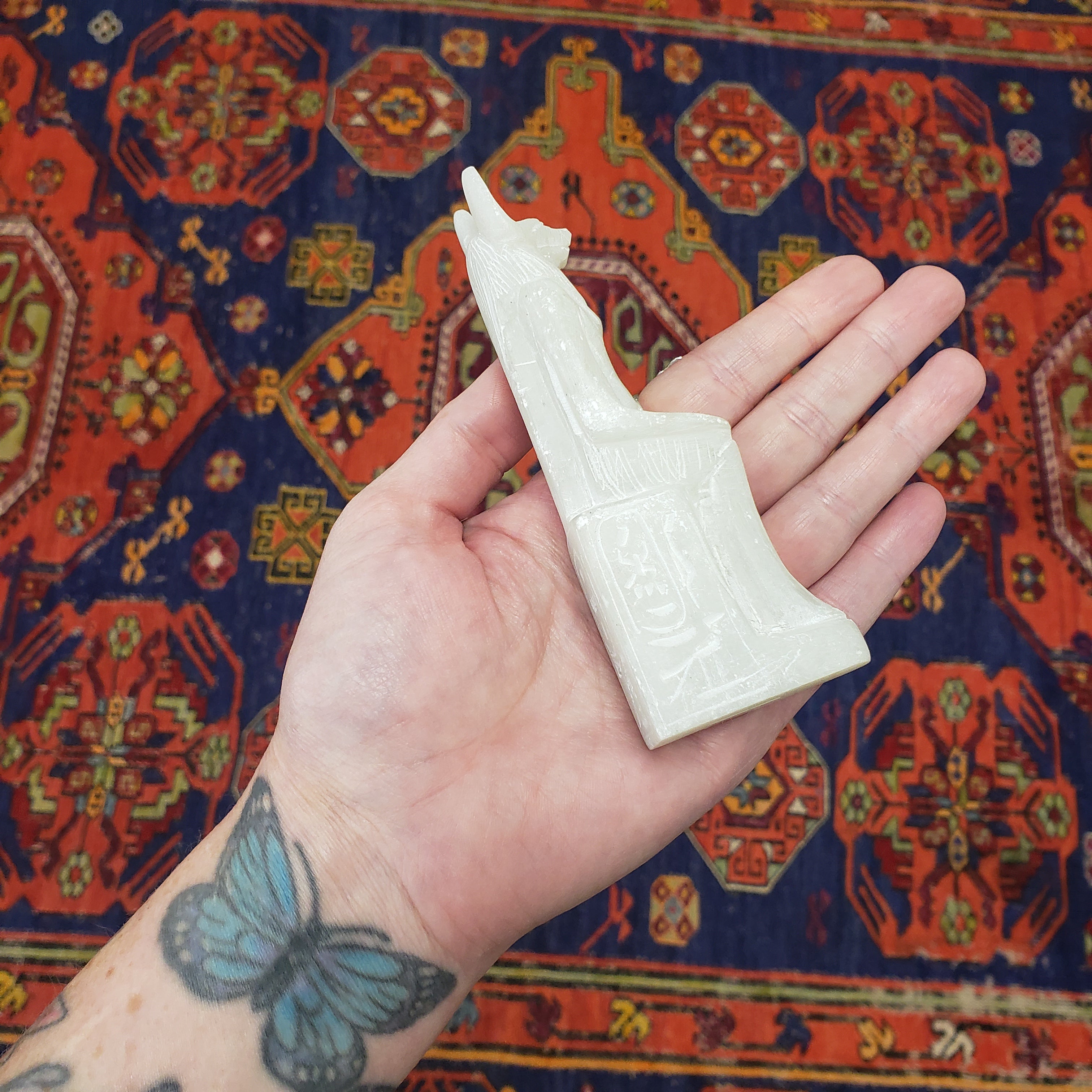Hand holding a white Anubis against a colorful patterned rug