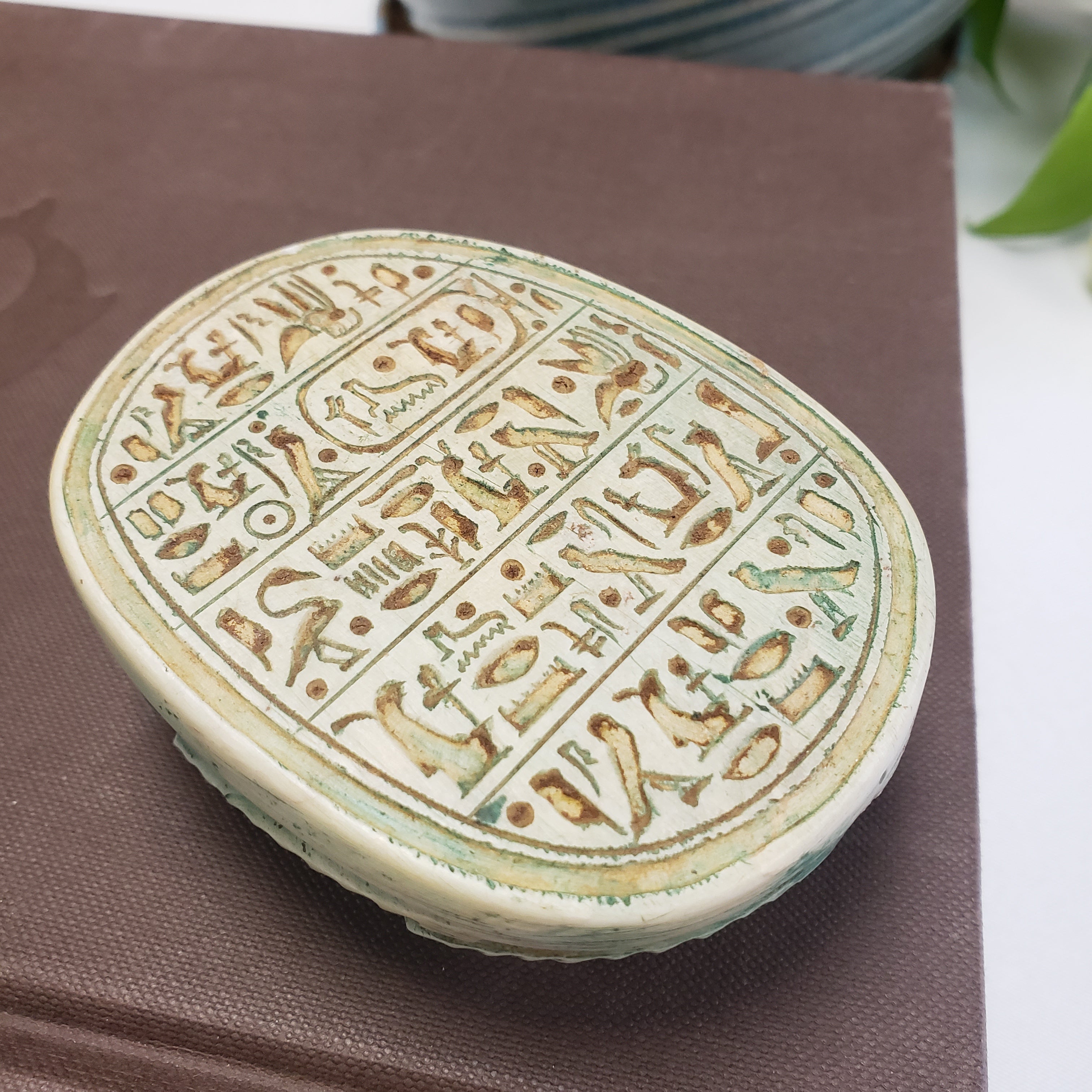 Round stone scarab with hieroglyphic carvings on a brown surface