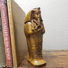 Decorative sculpture on top of books with a wooden shelf and white wall background