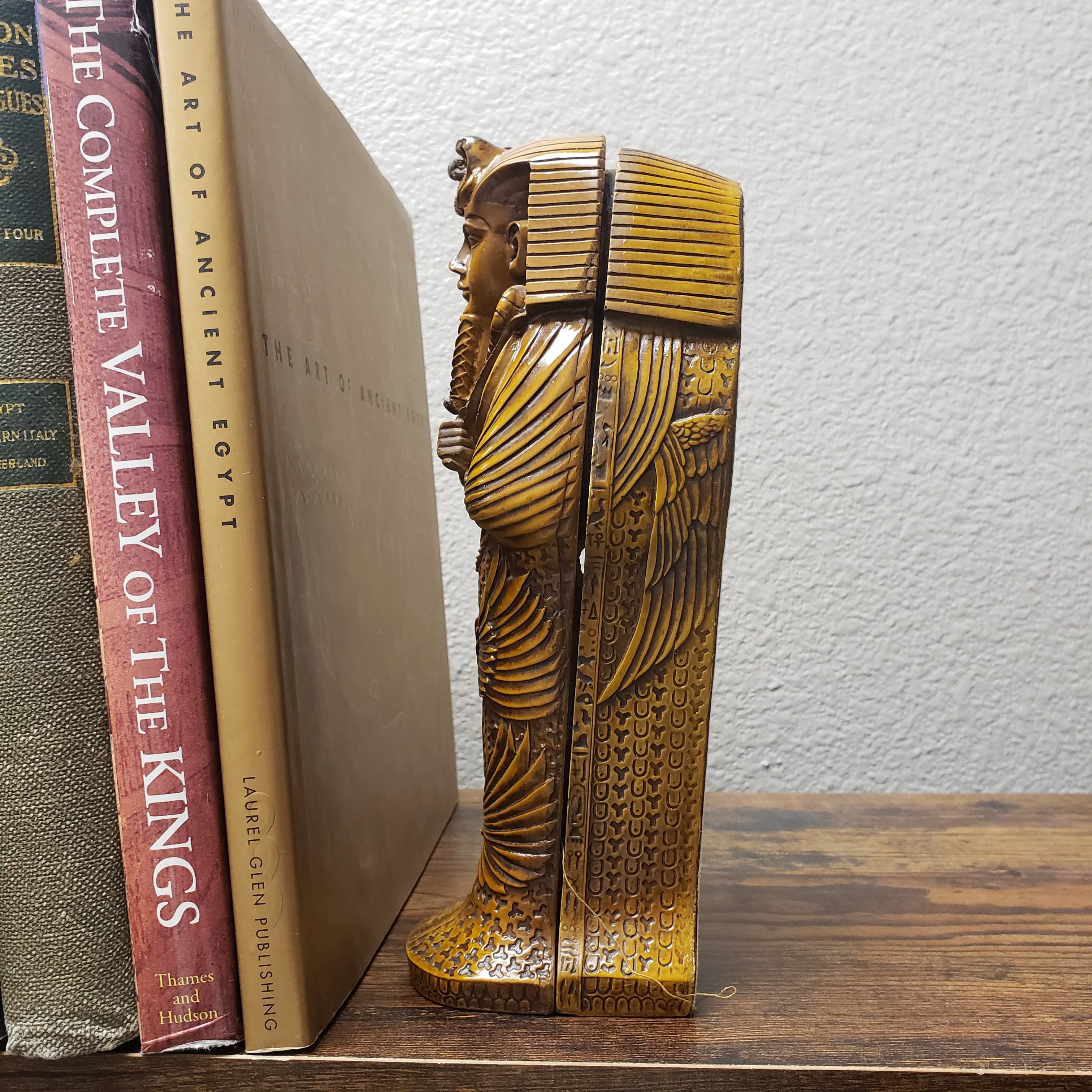 Decorative wooden shelf with carved design above books on a white wall.