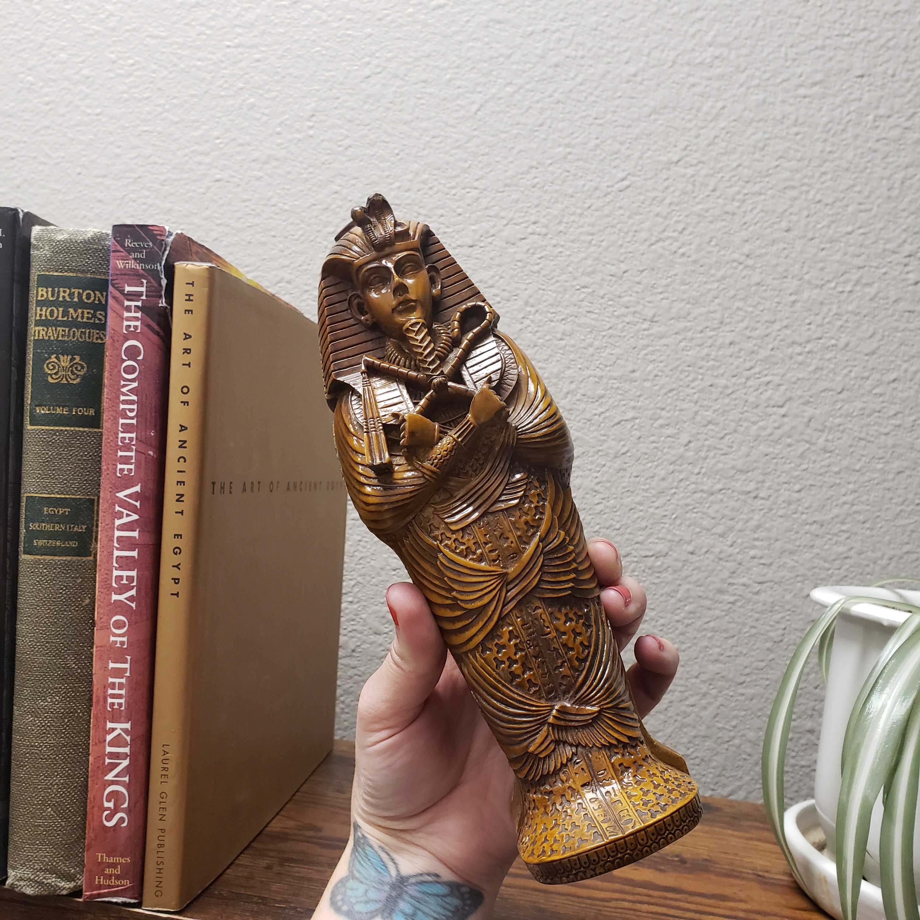 Hand holding a intricately carved wooden object over a stack of books on a white wall.
