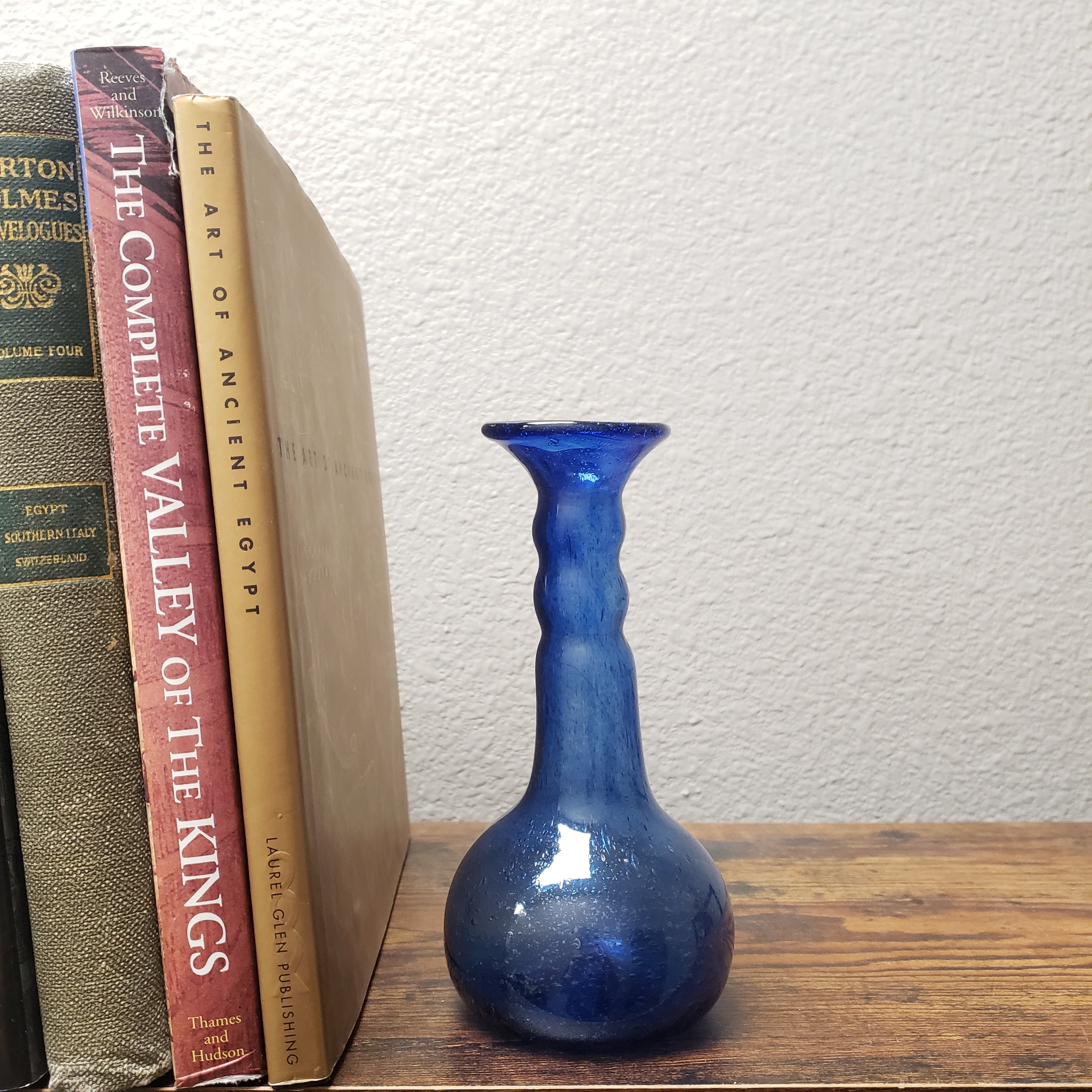 Blue vase on a stack of books with a white wall and wooden shelf background