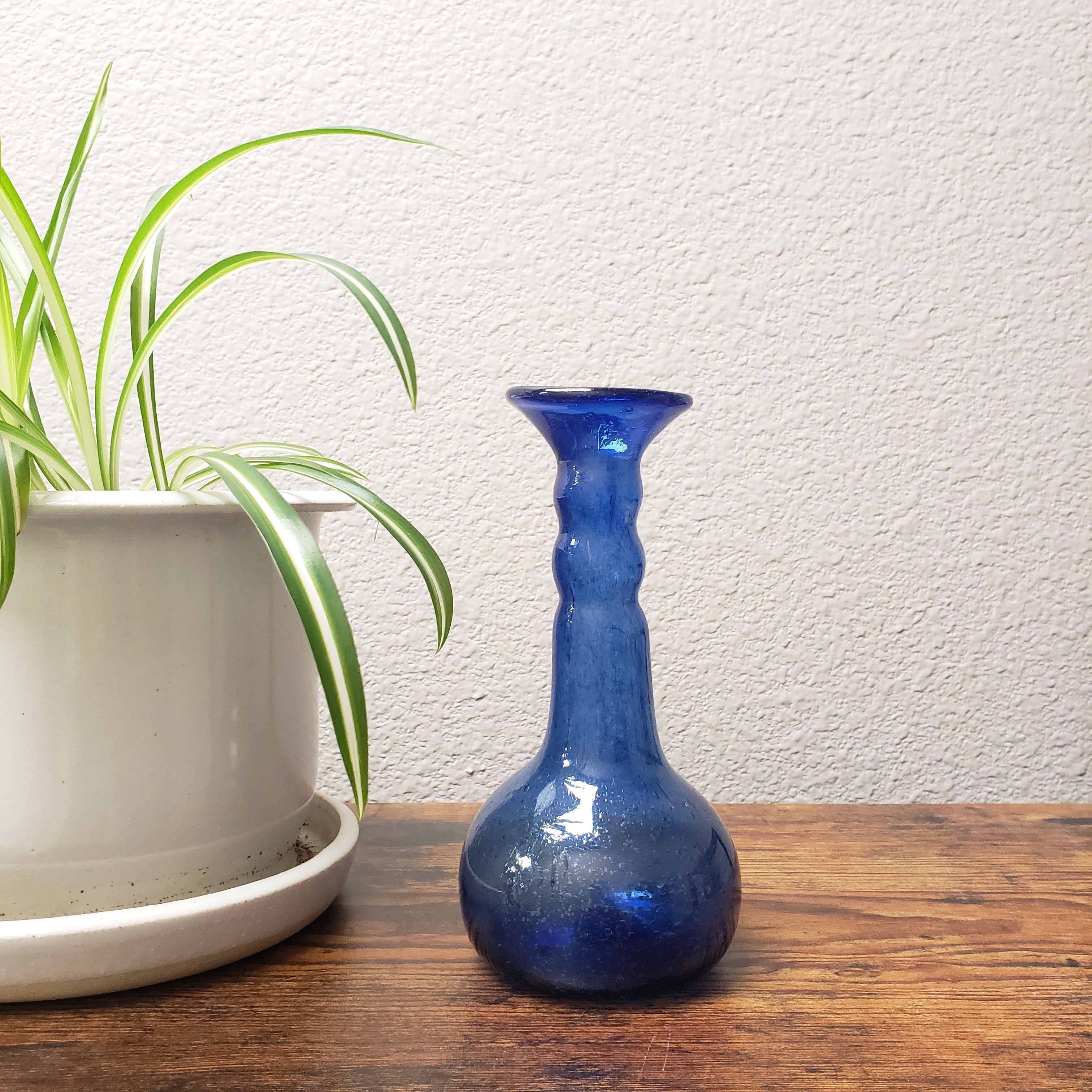 Blue glass vase leaning against a wooden surface with a white wall background
