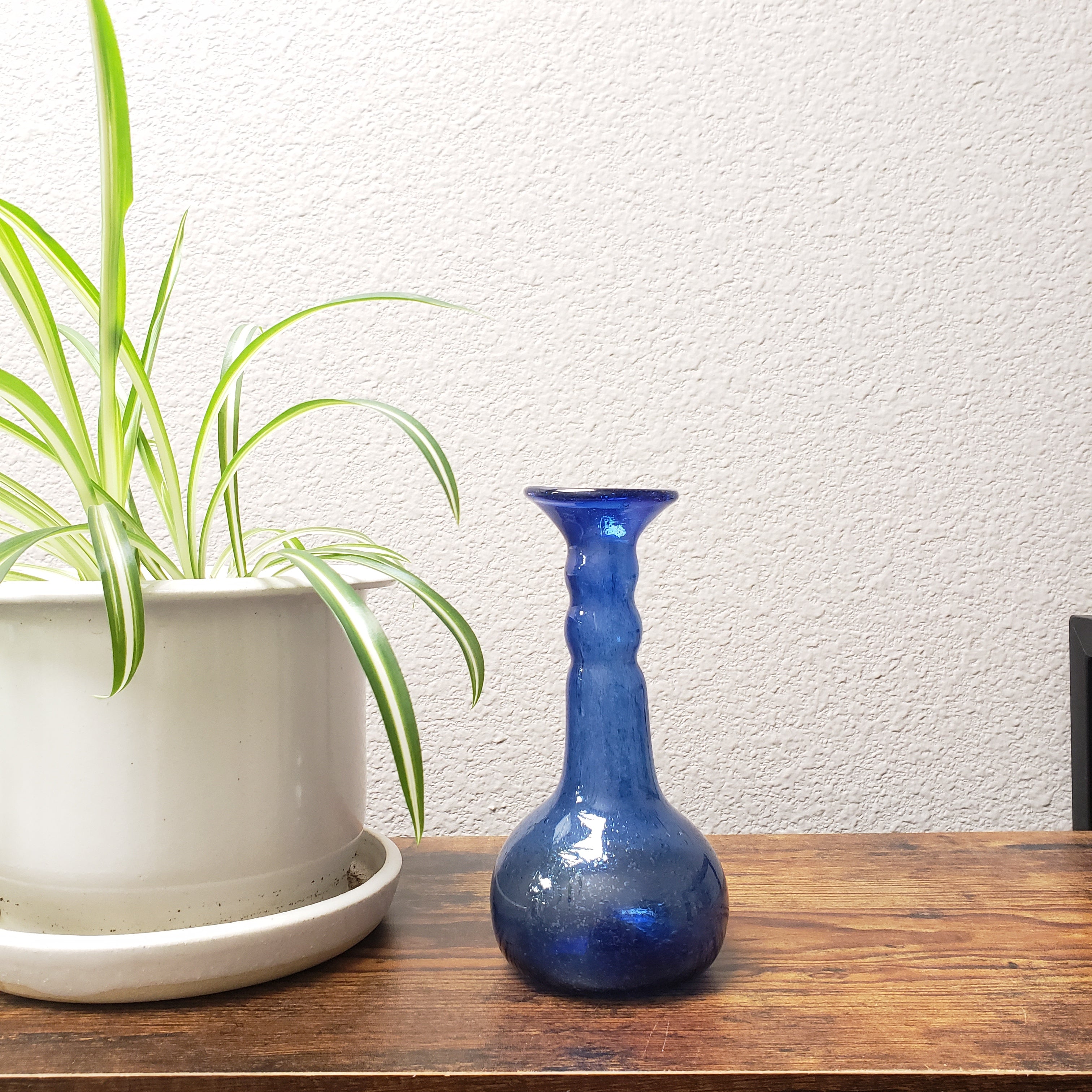 Blue ceramic vase on a wooden shelf with a white wall background