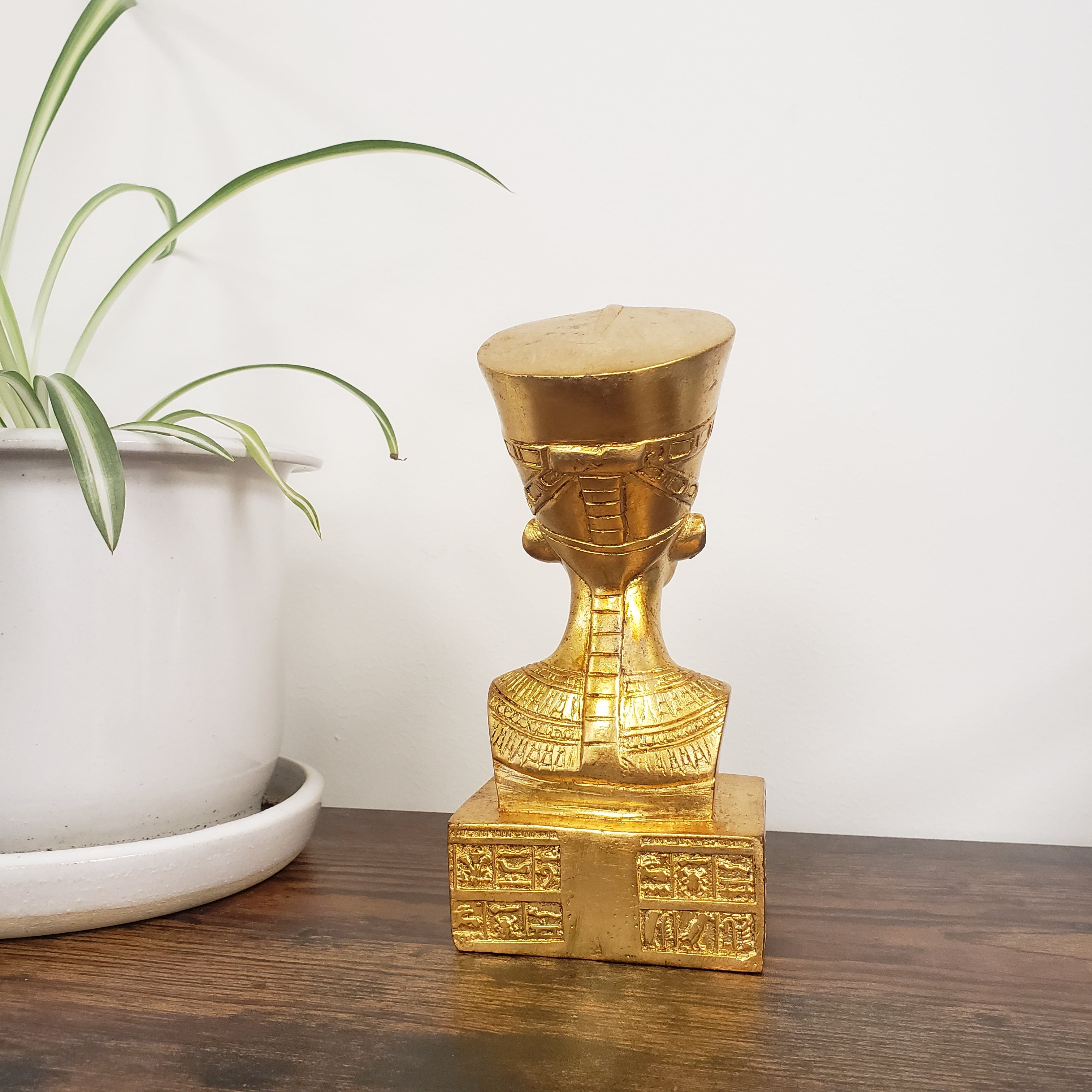 Gold decorative object on a wooden surface with a plant in the background