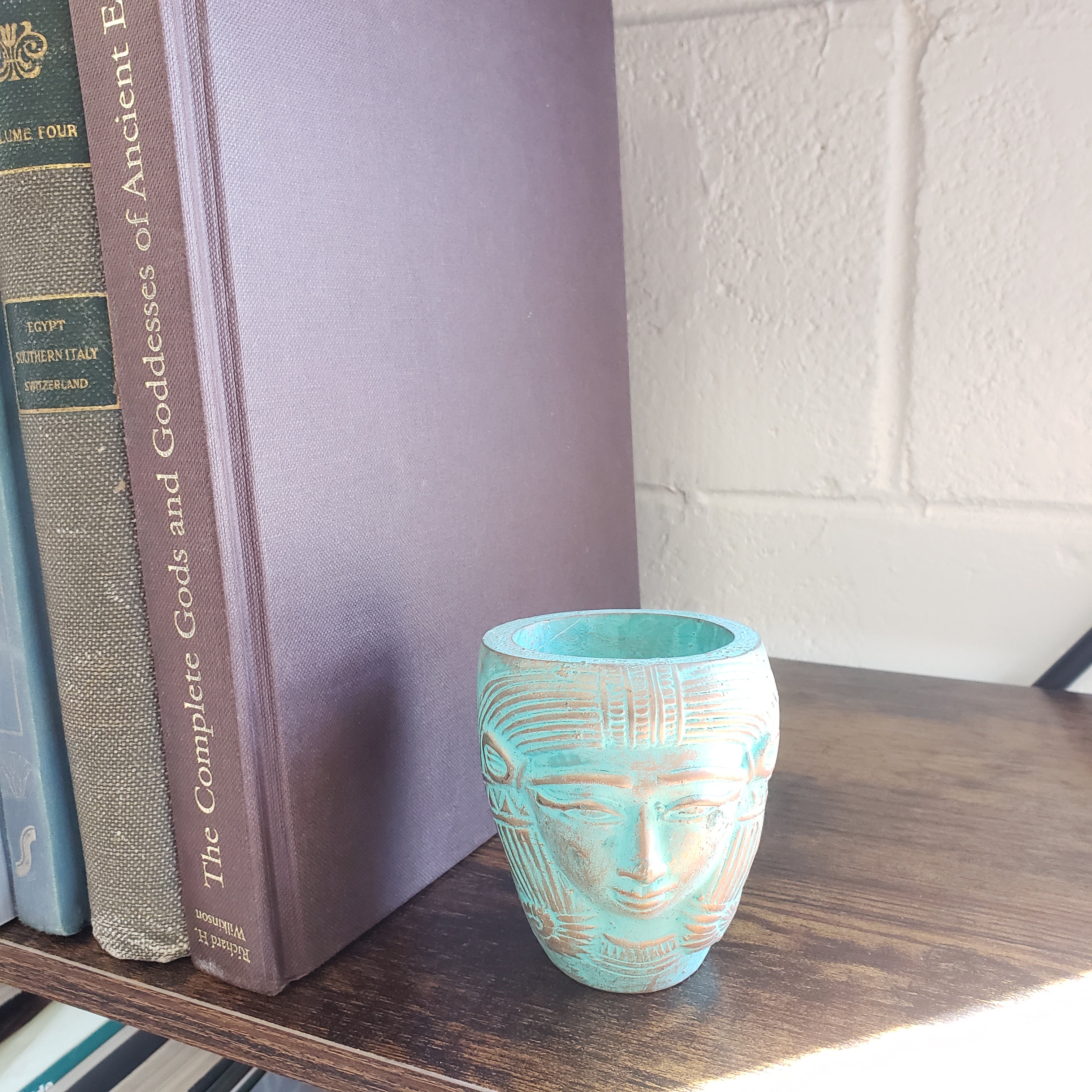 Turquoise decorative object on a stack of books with a wooden surface and white wall in the background