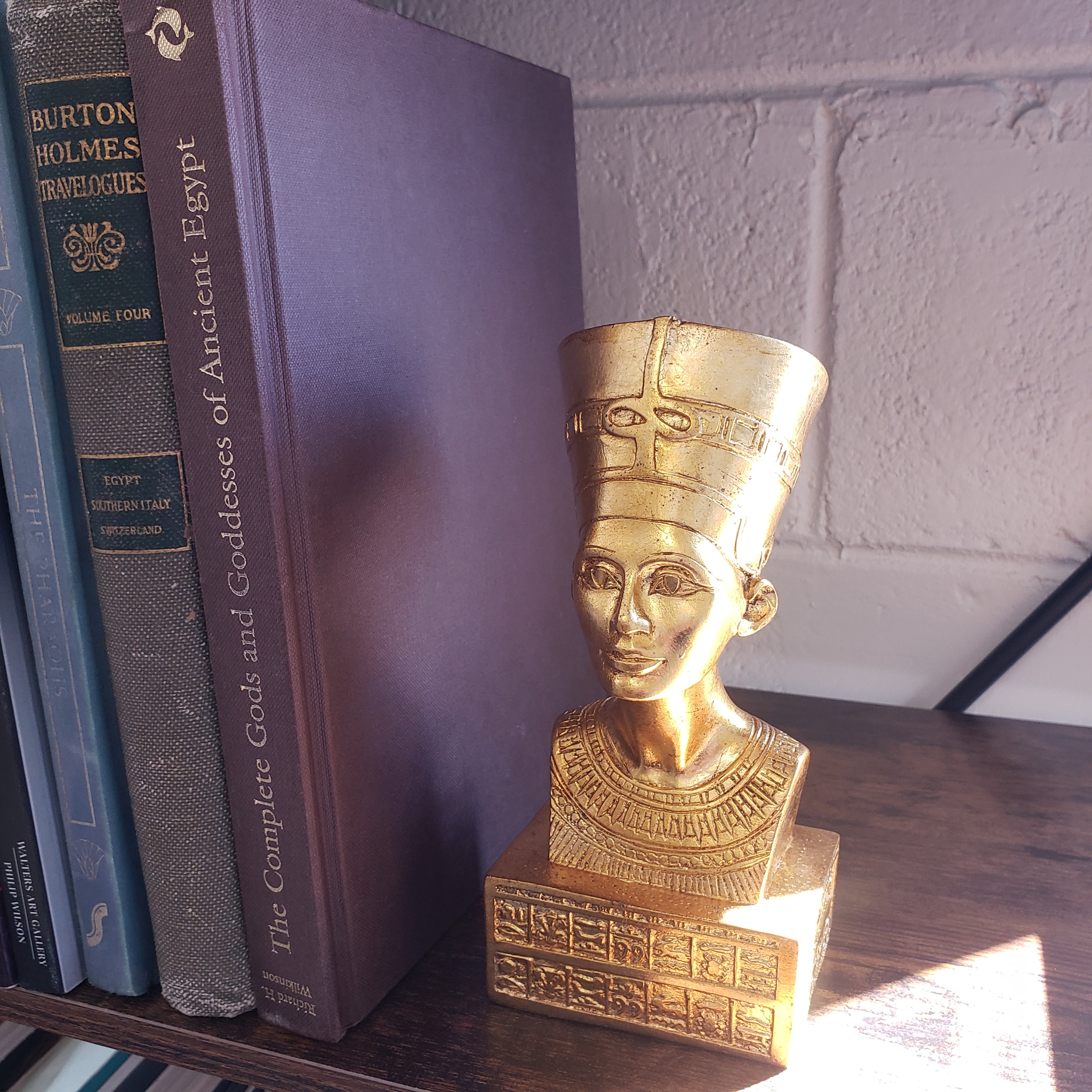 Gold bust of an Egyptian deity next to books on a shelf.