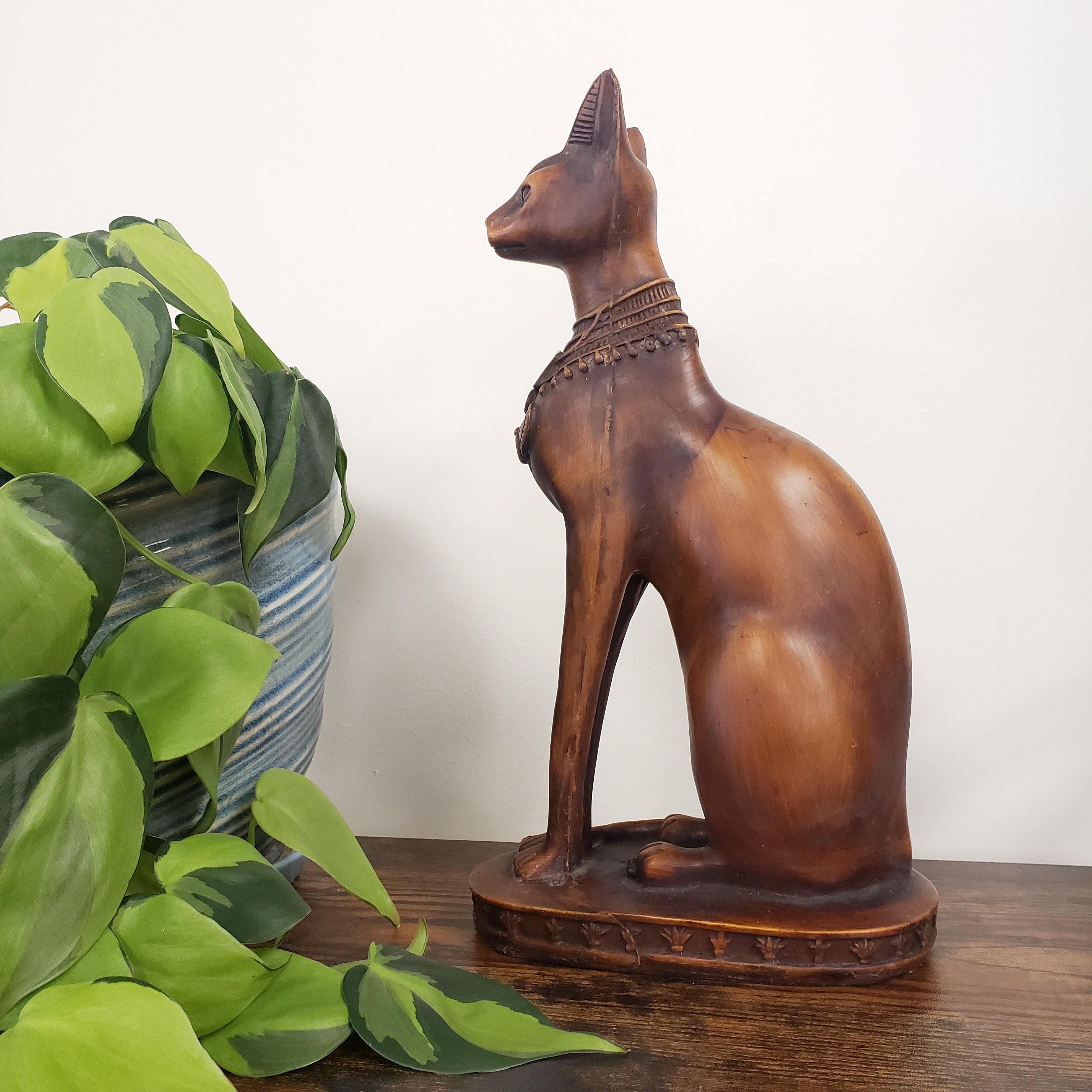 Wooden cat sculpture on a white background with green leaves in the foreground