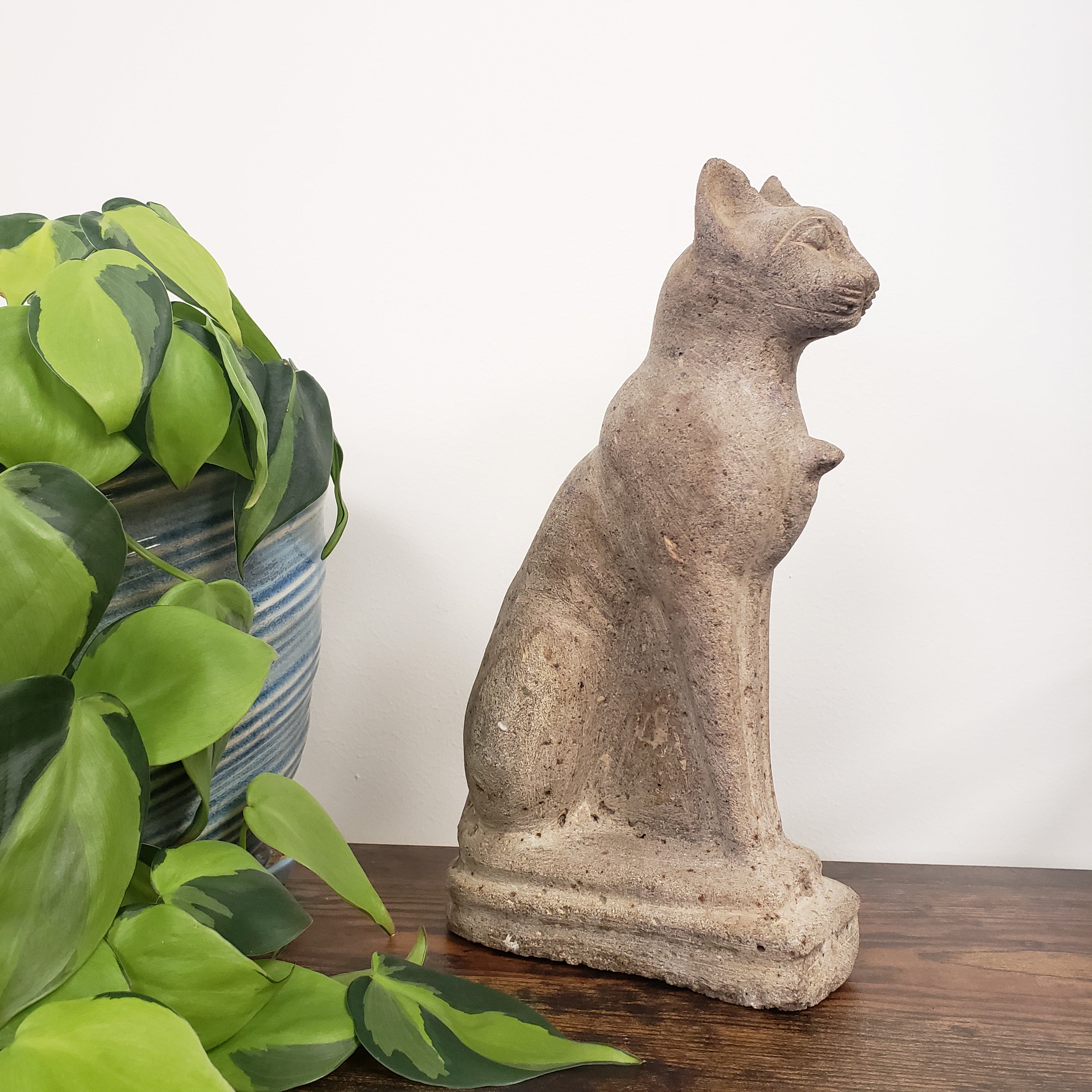 Decorative stone cat sculpture on a wooden surface with green leaves in the foreground