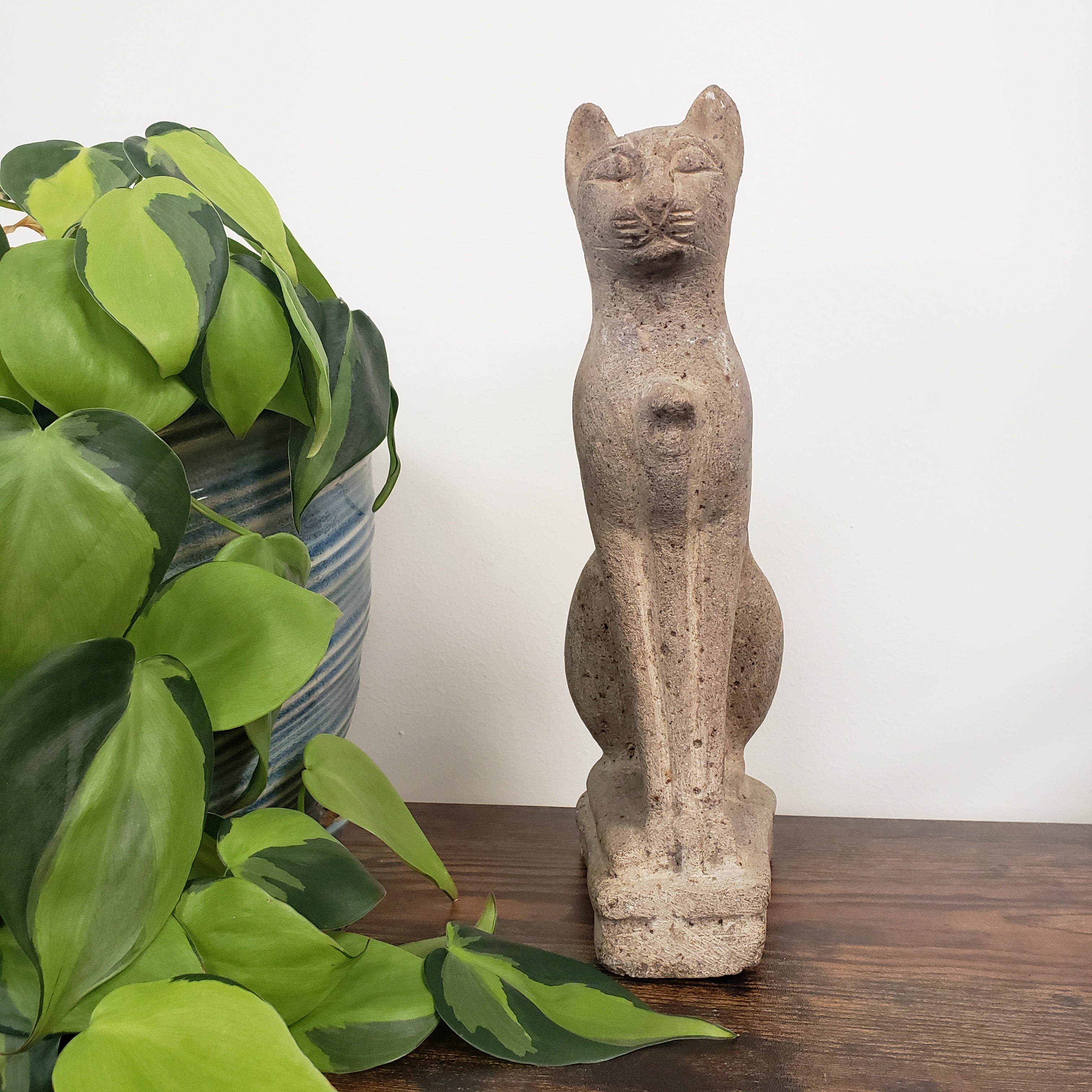 Decorative stone cat sculpture on a wooden surface with green plants in the foreground