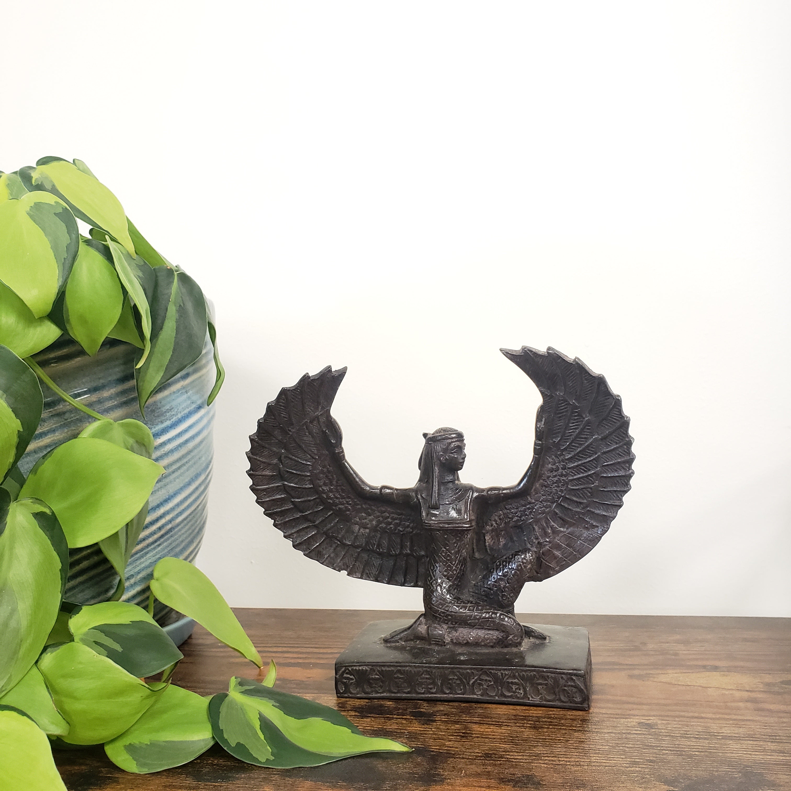 Decorative Egyptian Isis statue on a wooden board with green leaves.