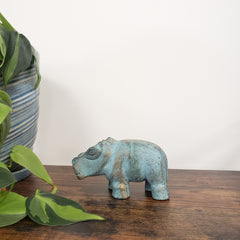 Decorative hippo statue on a wooden board with plants in the background