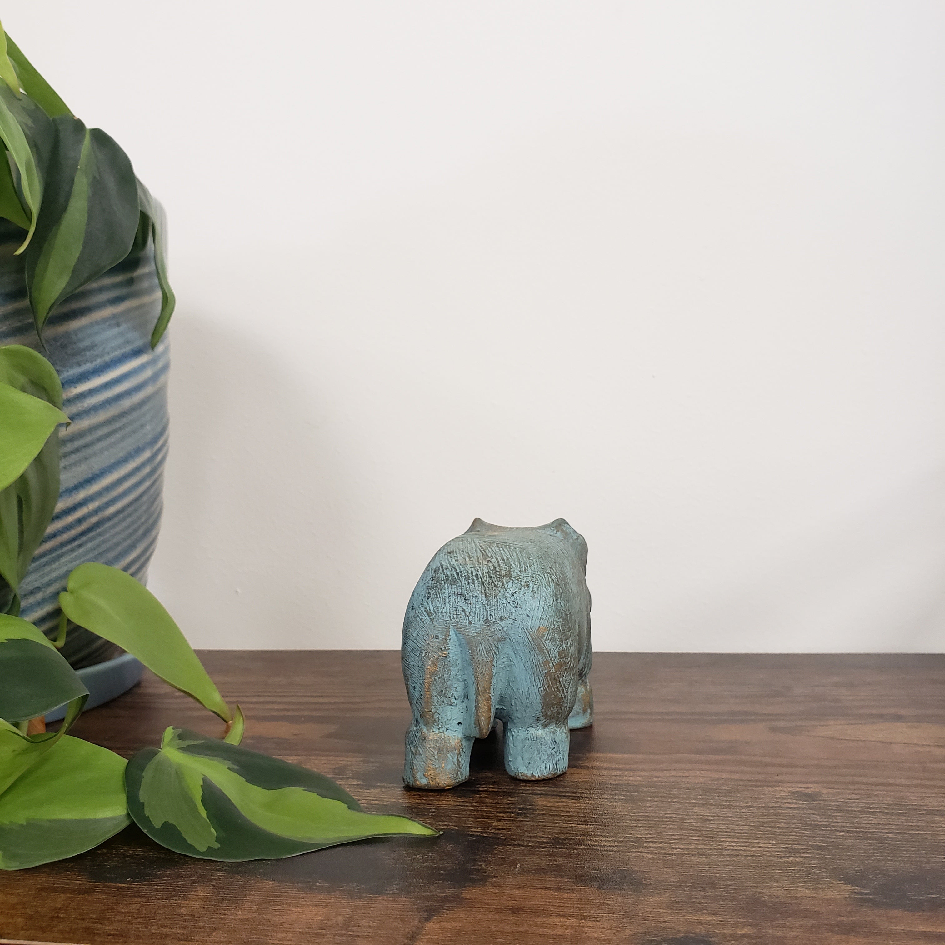 Decorative green hippo statue sculpture on a wooden surface with plants in the foreground.