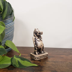 Decorative Egyptian hippo goddess sculpture on a wooden surface with plants in the foreground.