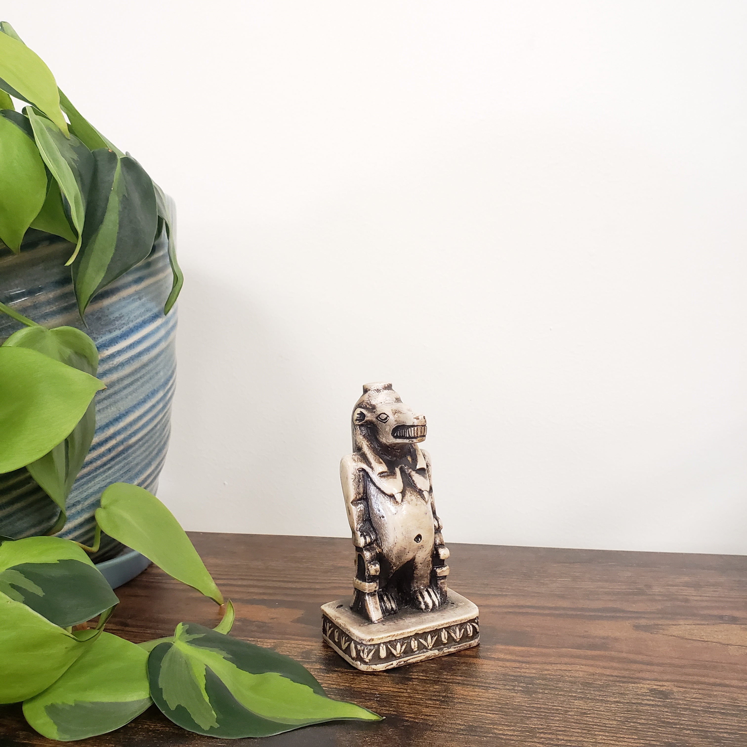 Decorative Egyptian hippo goddess on a wooden door with green leaves in the foreground
