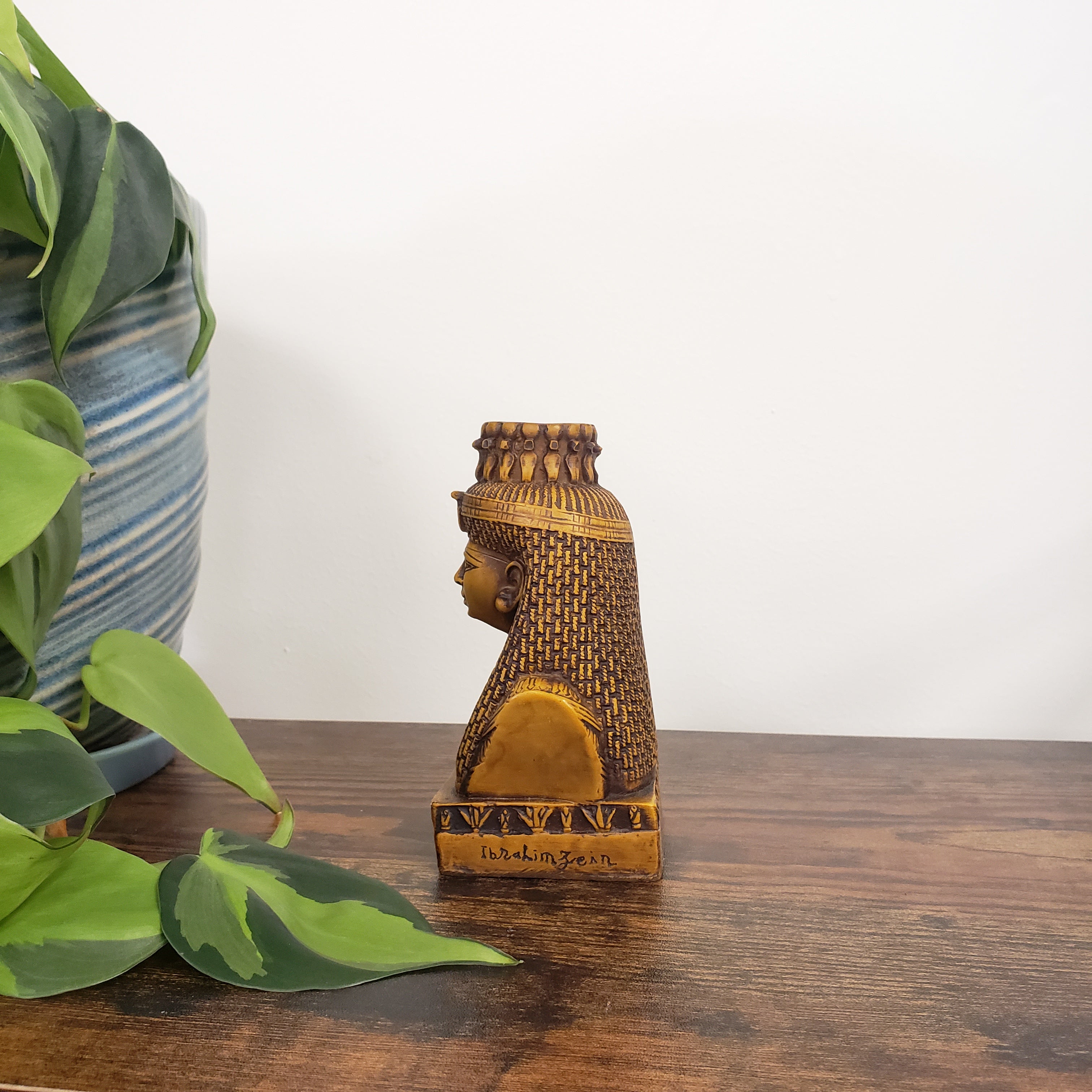 Decorative Egyptian Queen Mutnejmet Statue on a wooden surface with plants in the foreground.