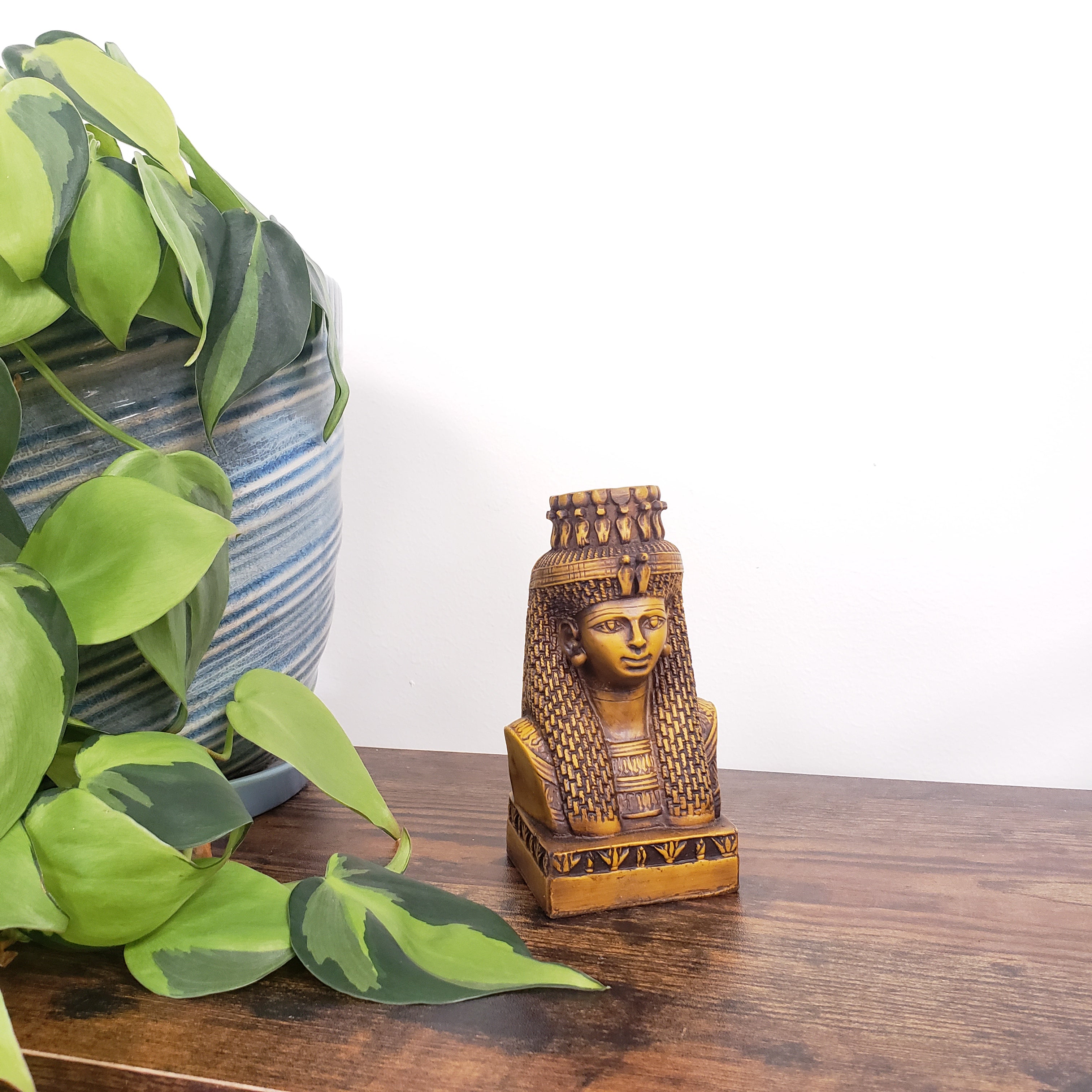 Decorative Egyptian Queen Mutnejmet Statue with green leaves and striped fabric in the background