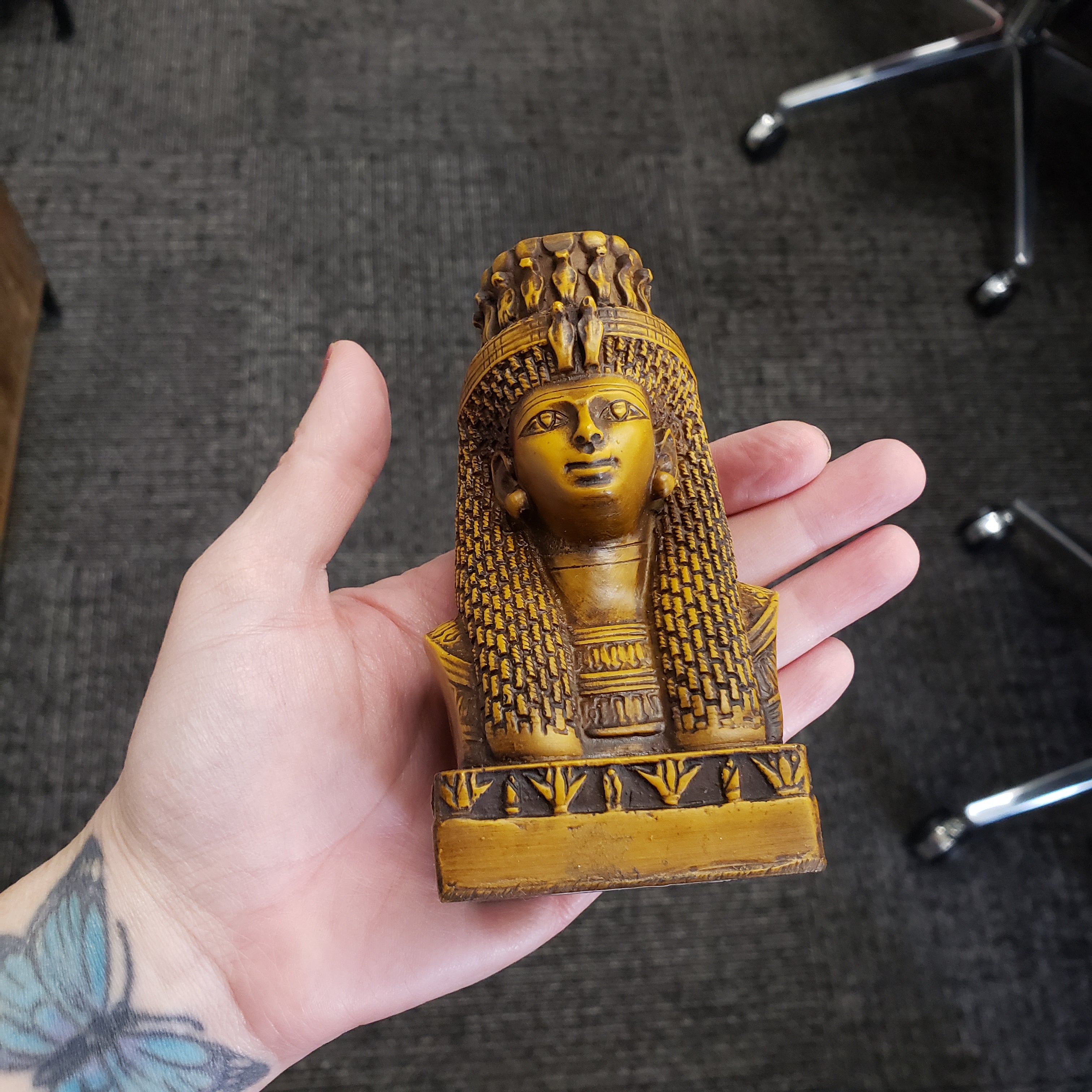 Hand holding a intricately carved Egyptian Queen Mutnejmet Statue on a carpeted floor.