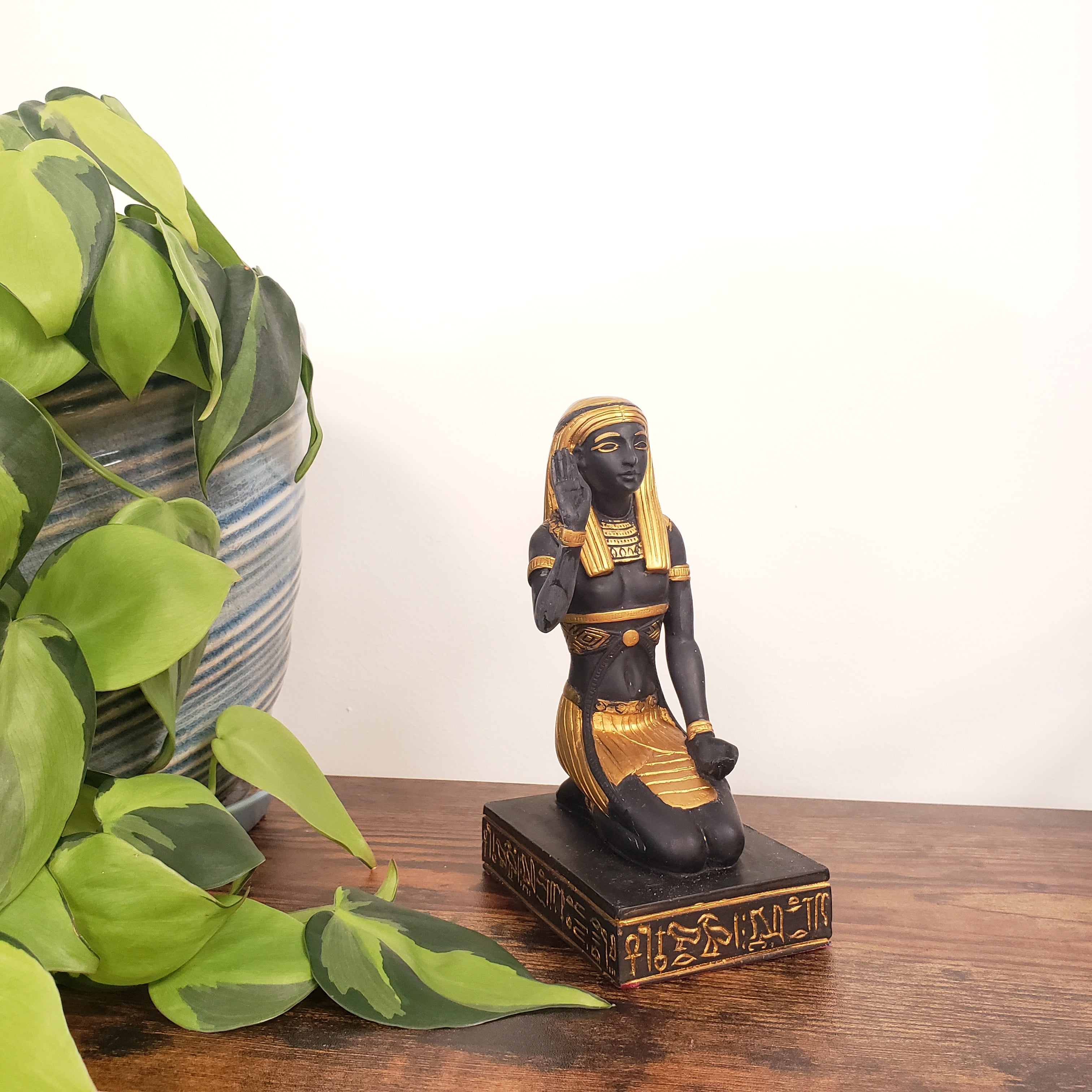 Decorative Egyptian statue with black and gold design on a wooden surface with green leaves.