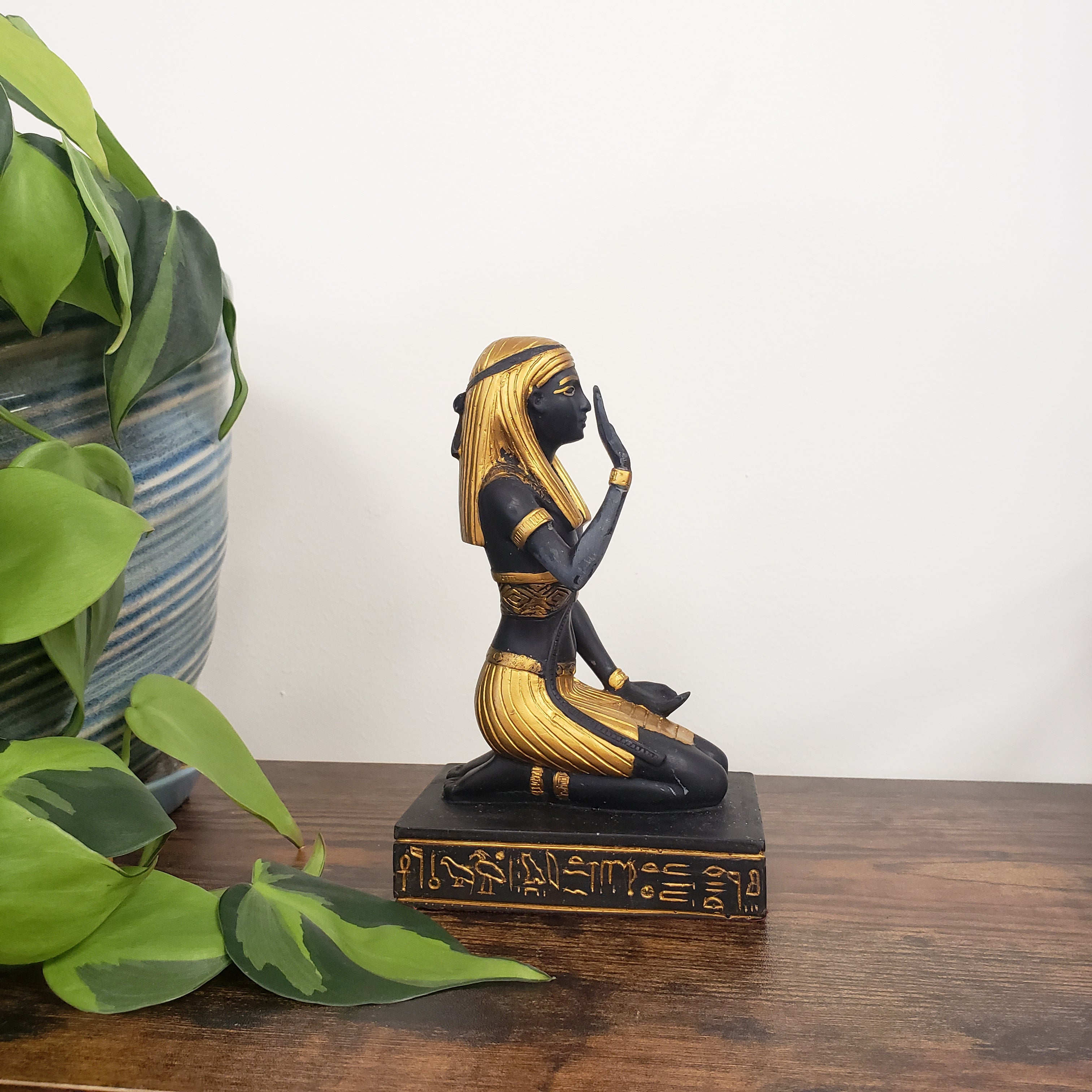 Decorative Egyptian statue with gold and black finish on a wooden board.