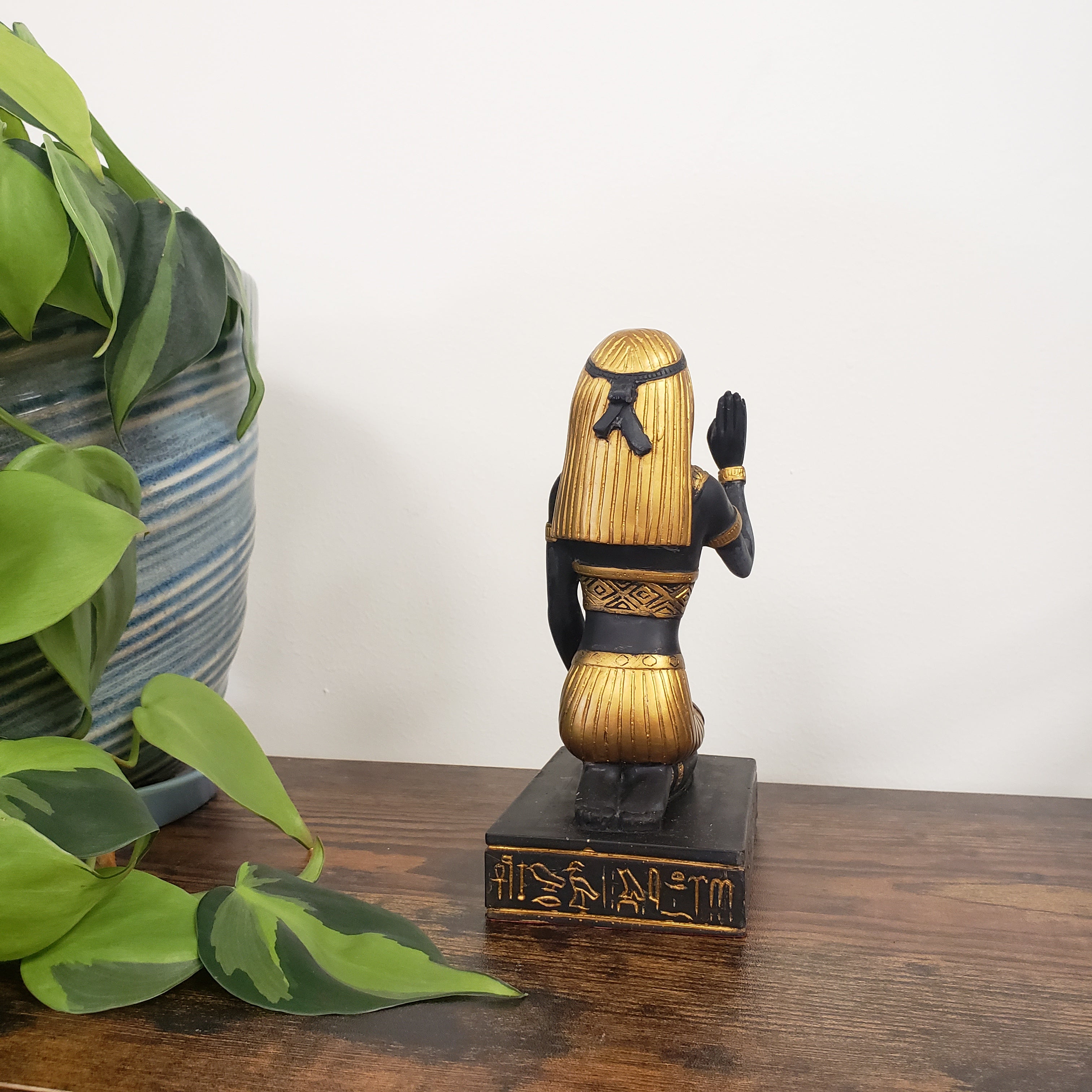 Decorative Egyptian statue on a wooden door with plants in the foreground.