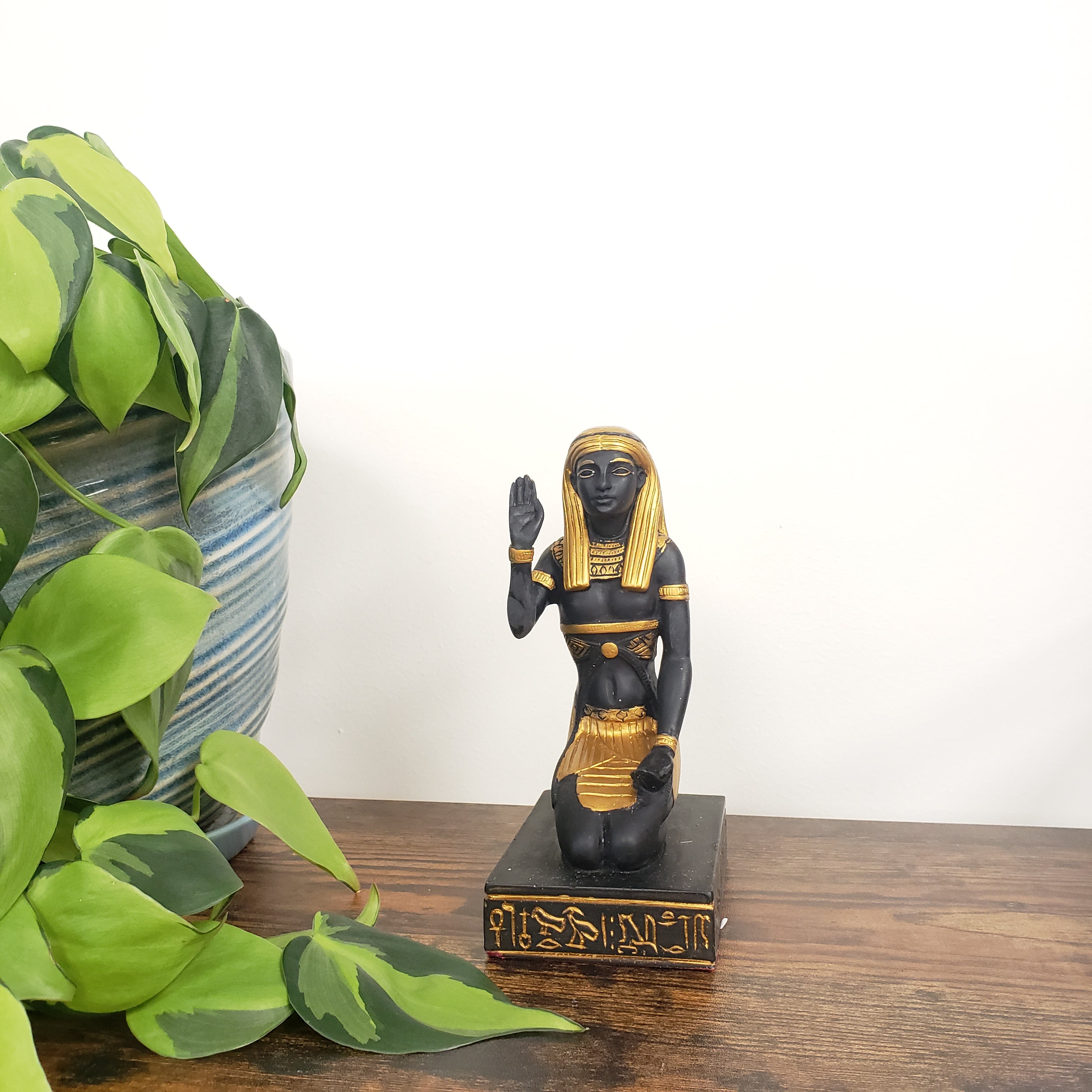 Decorative Egyptian statue with a black and gold design on a wooden door, surrounded by green leaves.