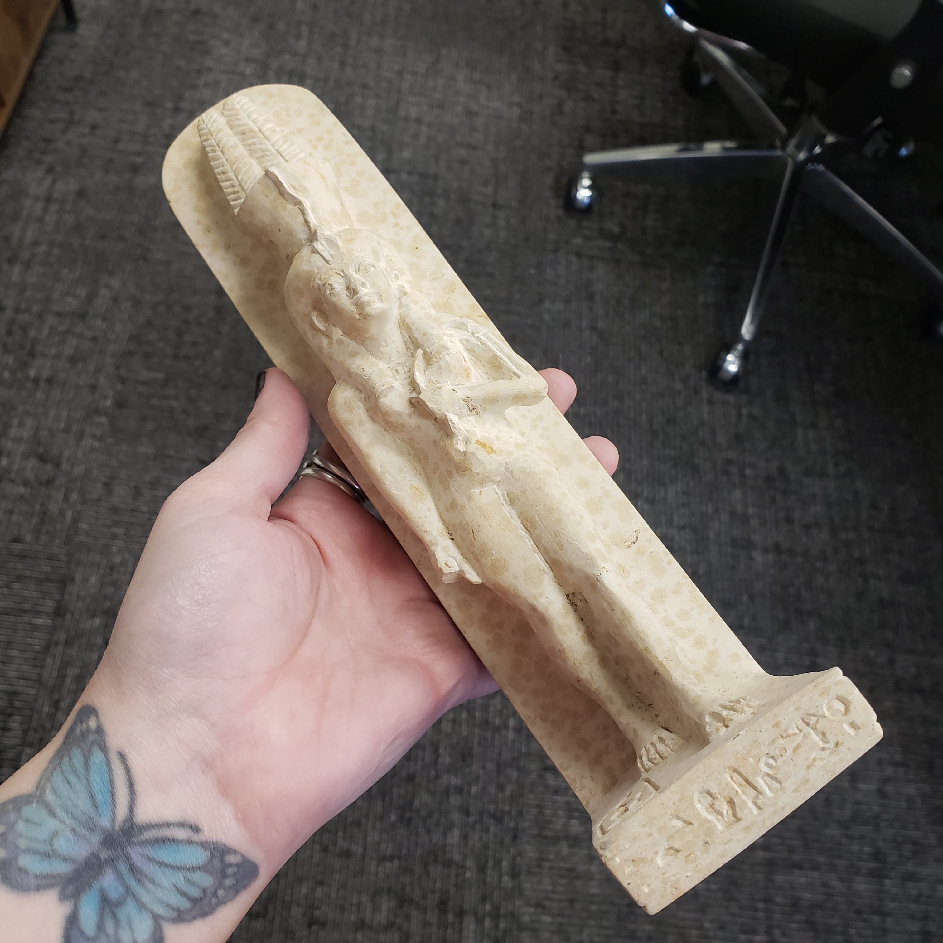 Hand holding a stone sculpture of a statue of Tiye figure on a dark textured surface