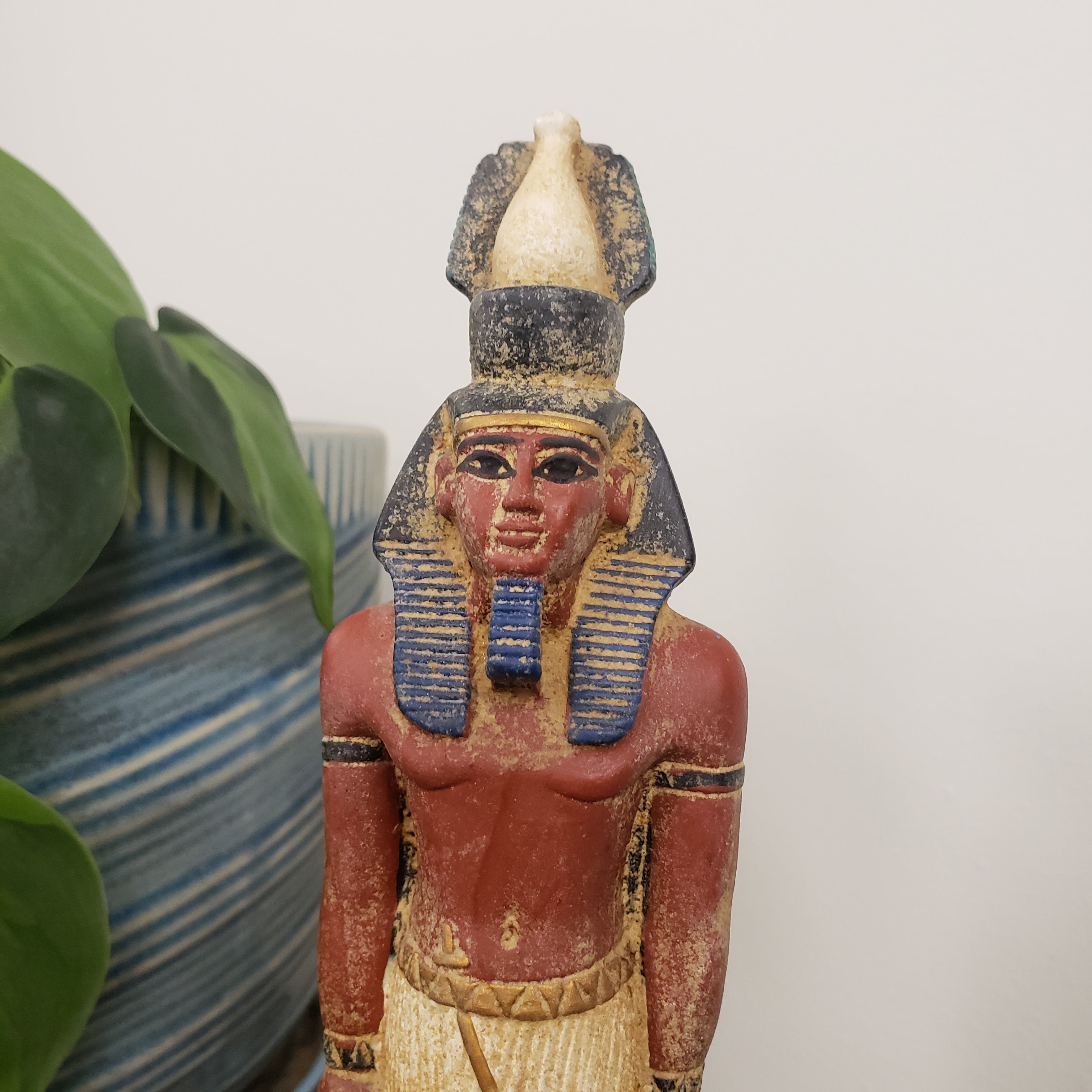 Decorative figure with a red face and red body on a striped surface with green leaves.