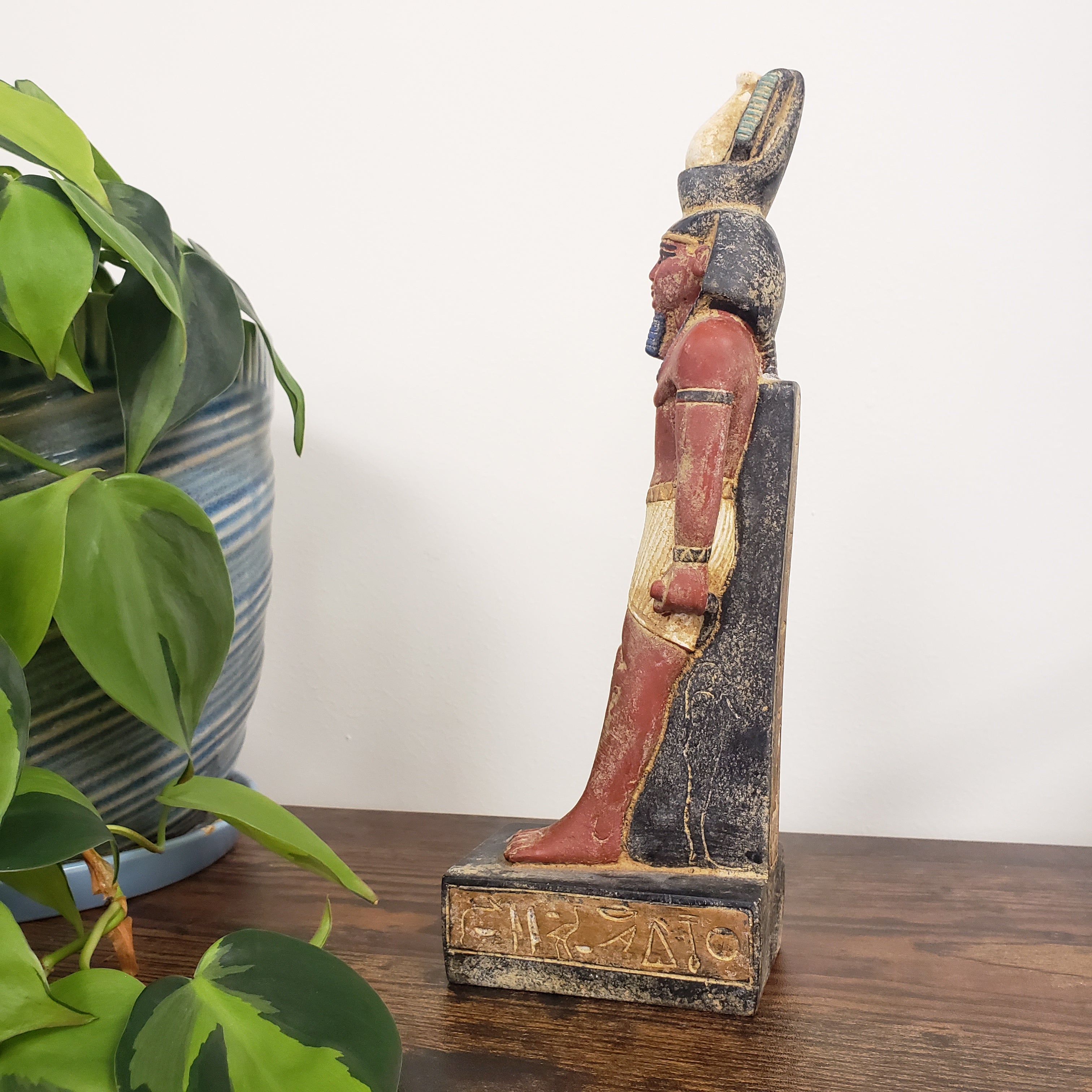 Decorative Egyptian Ramses statue on a wooden surface with plants in the foreground