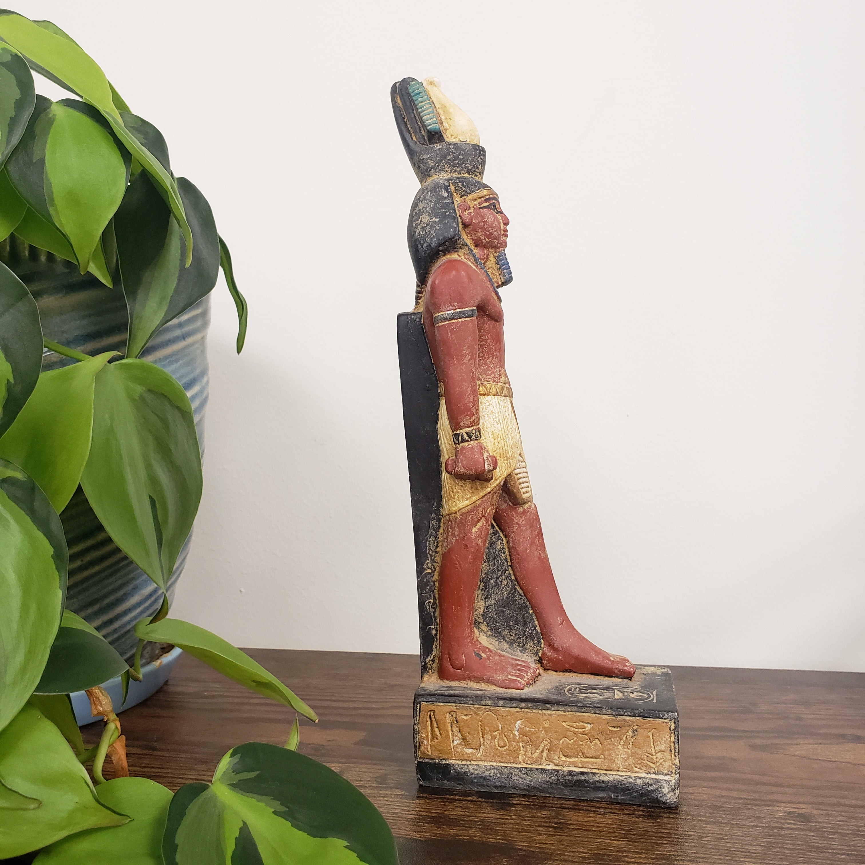 Decorative statue of Egyptian Ramses  on a wooden base with plants in the foreground