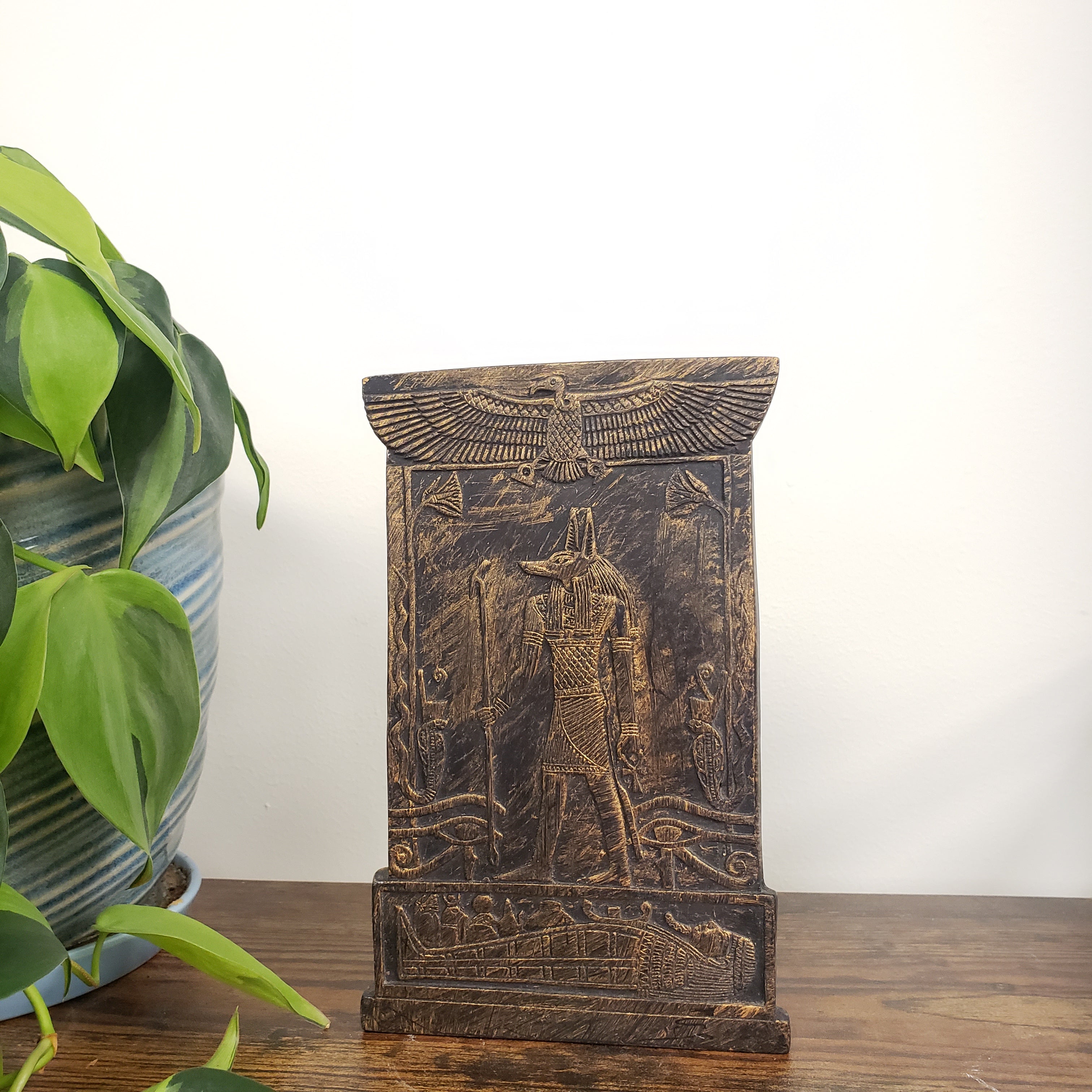 Decorative Anubis plaque with intricate carvings on a white wall.