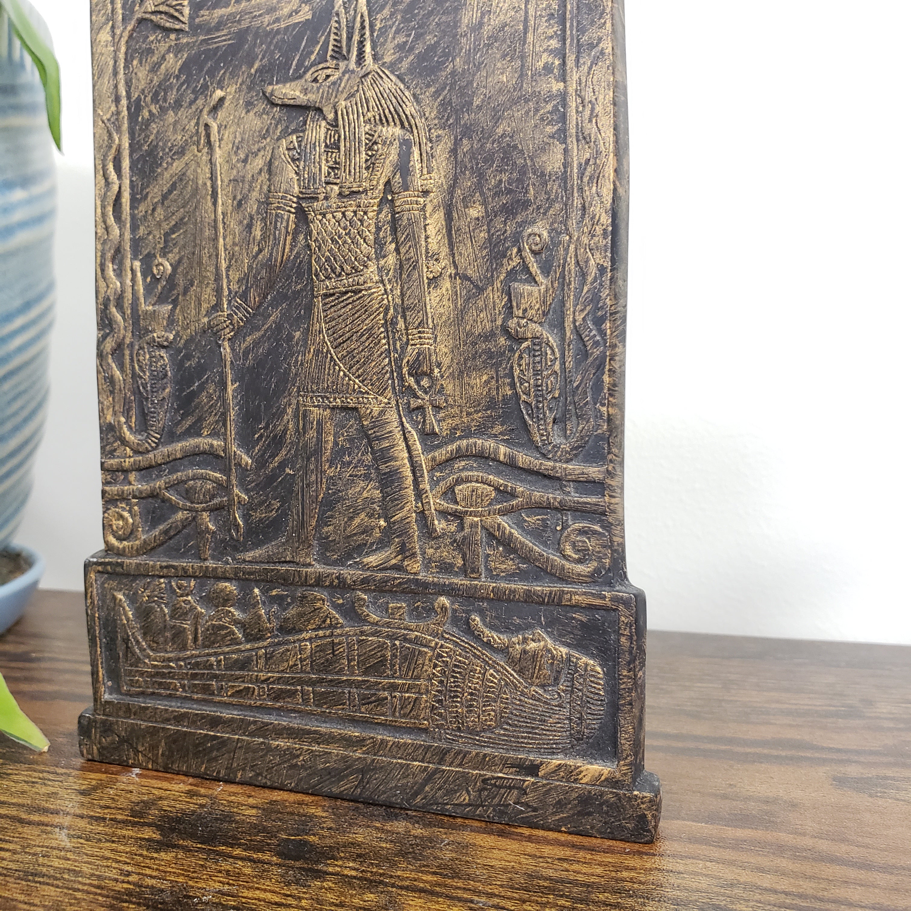 Decorative Anubis plaque with intricate carvings of a warrior and a sphinx on a wooden surface.