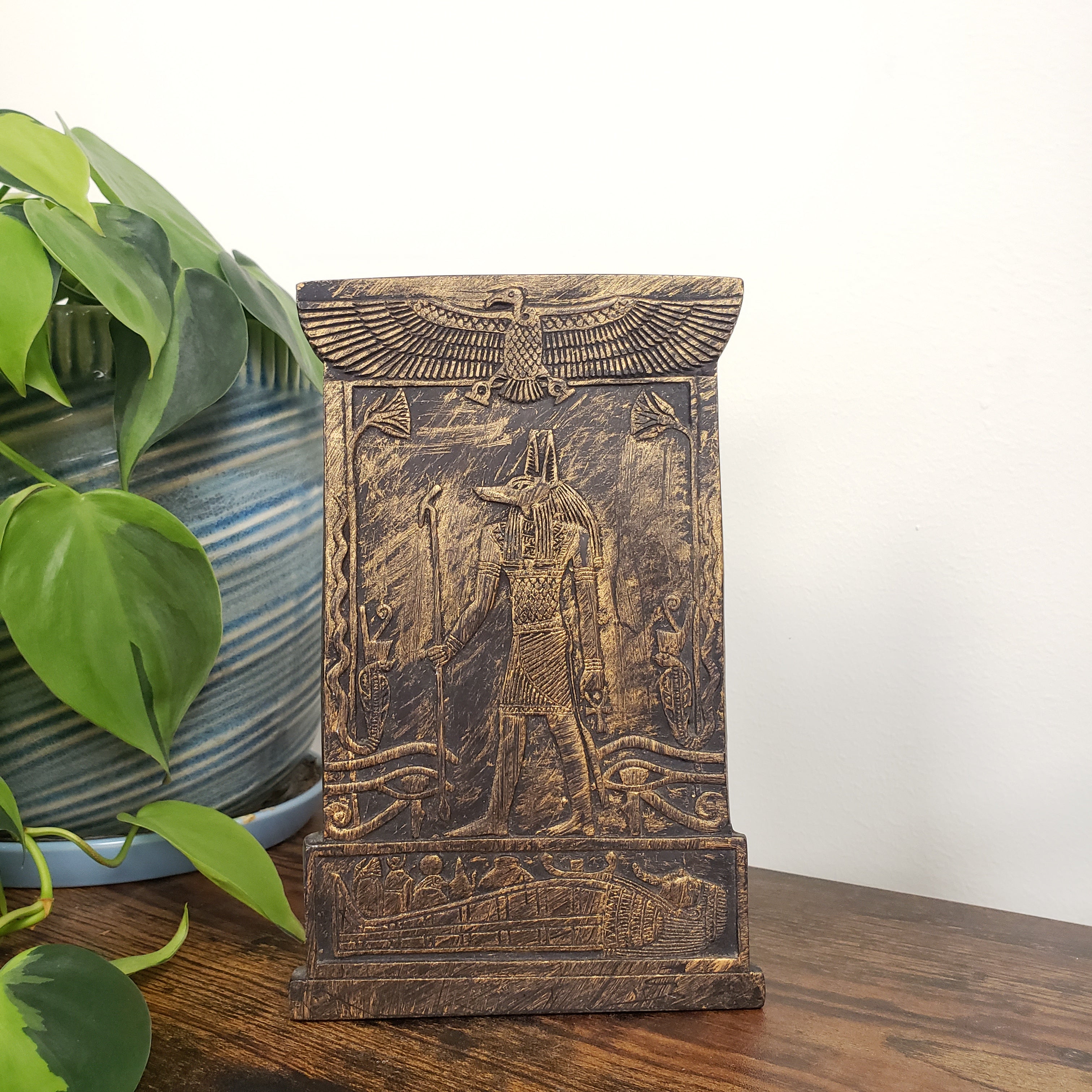 Decorative Anubis plaque with engraved design on a white wall with plants.