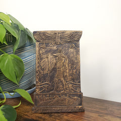 Decorative Anubis plaque with engraved design on a white wall with plants.