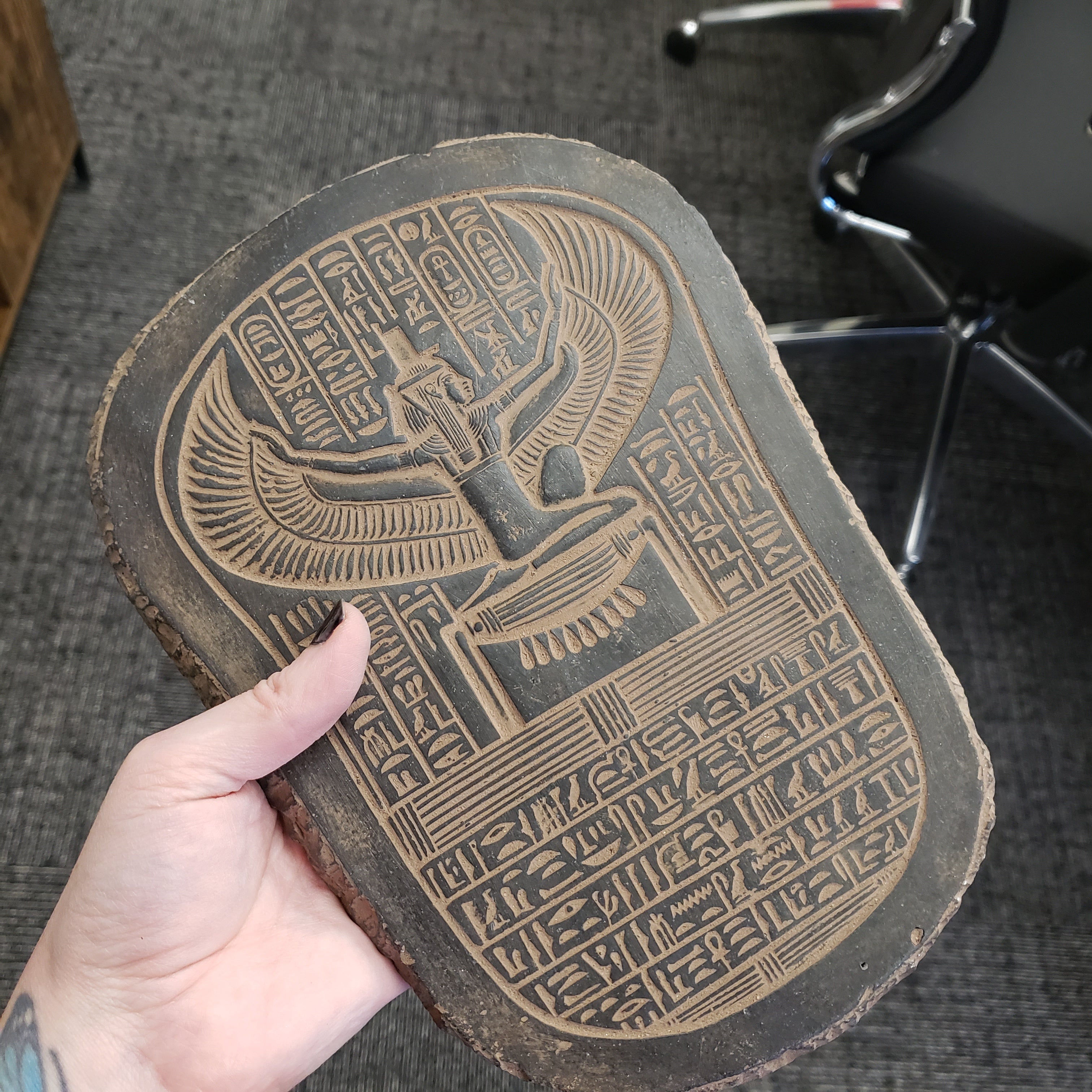 Hand holding a wooden block with hieroglyphics and an Egyptianiform figure.